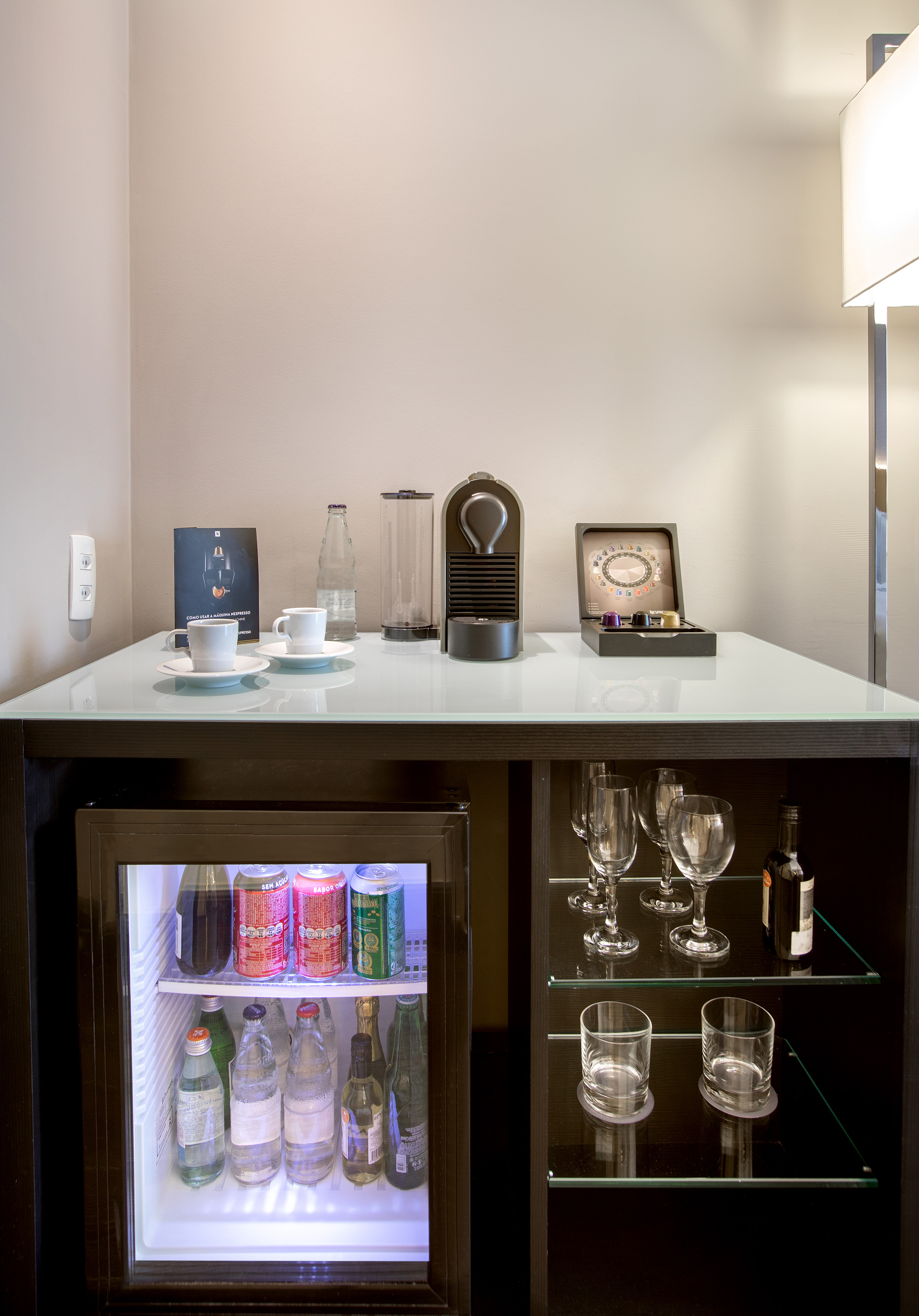 Hotel minibar with Nespresso coffee machine, assorted beverages, and glassware.