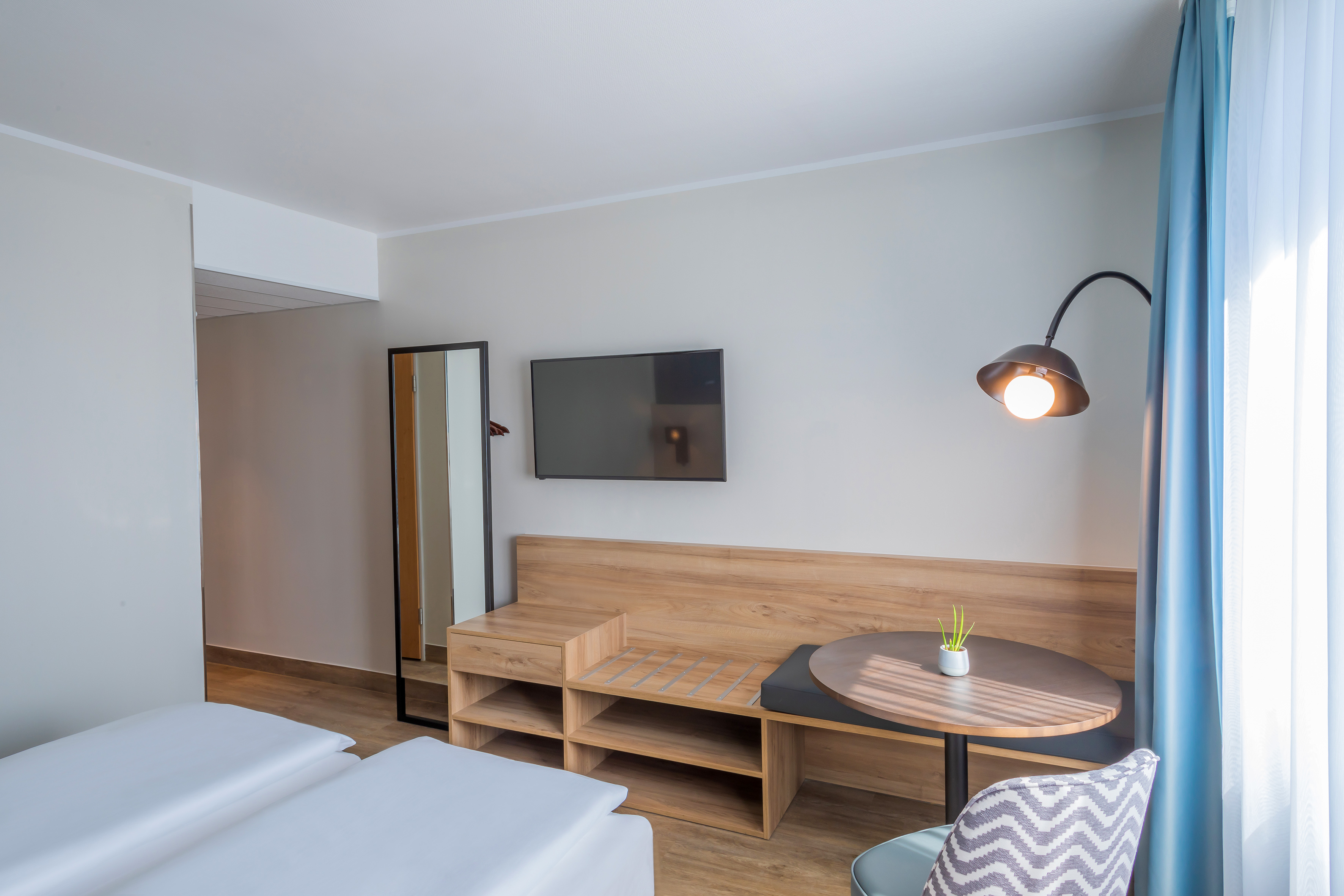 Stylish hotel room with twin beds, TV, wooden bench, and cozy dining area.