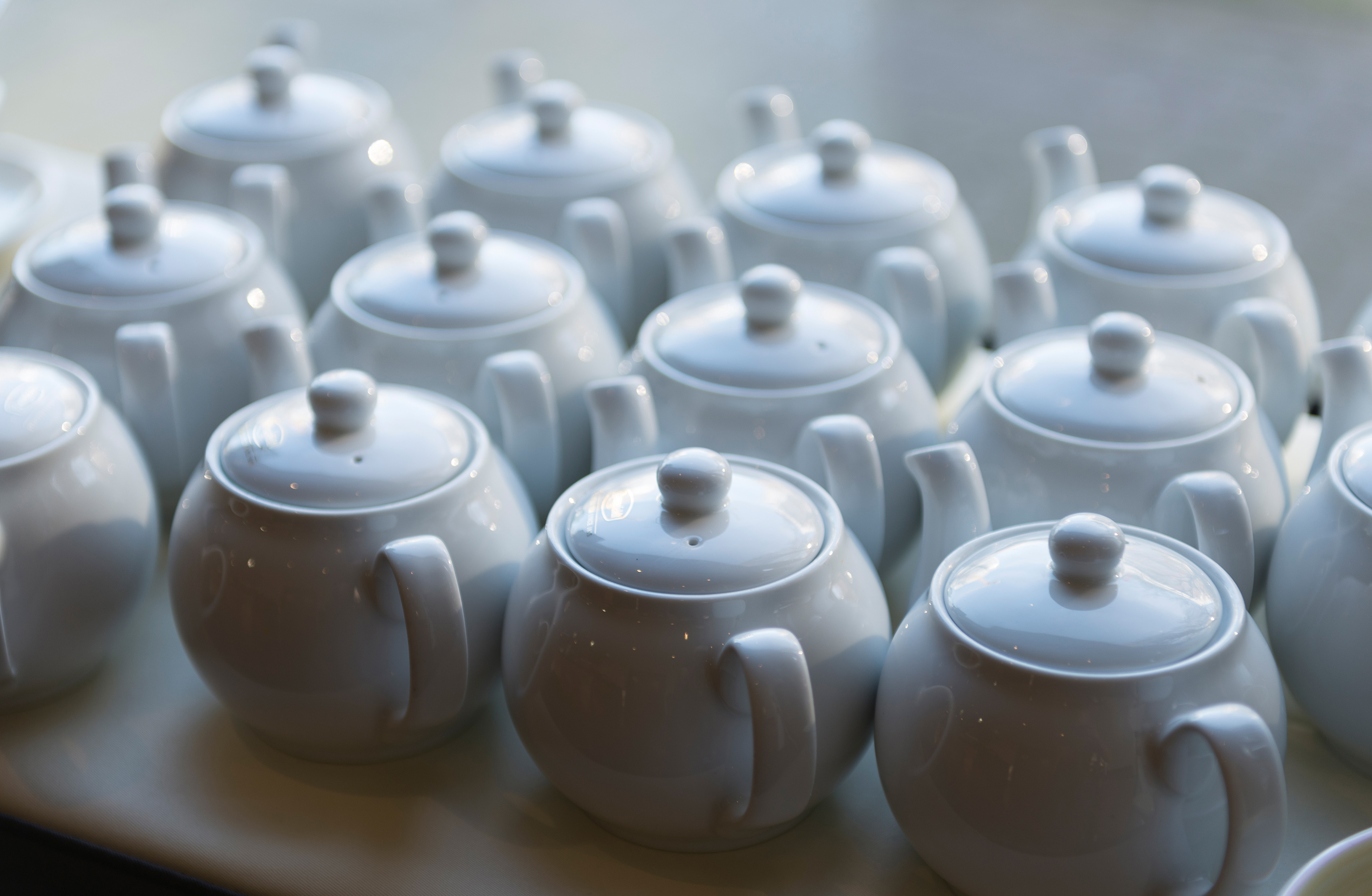 Row of elegant white ceramic teapots ready for tea service.
