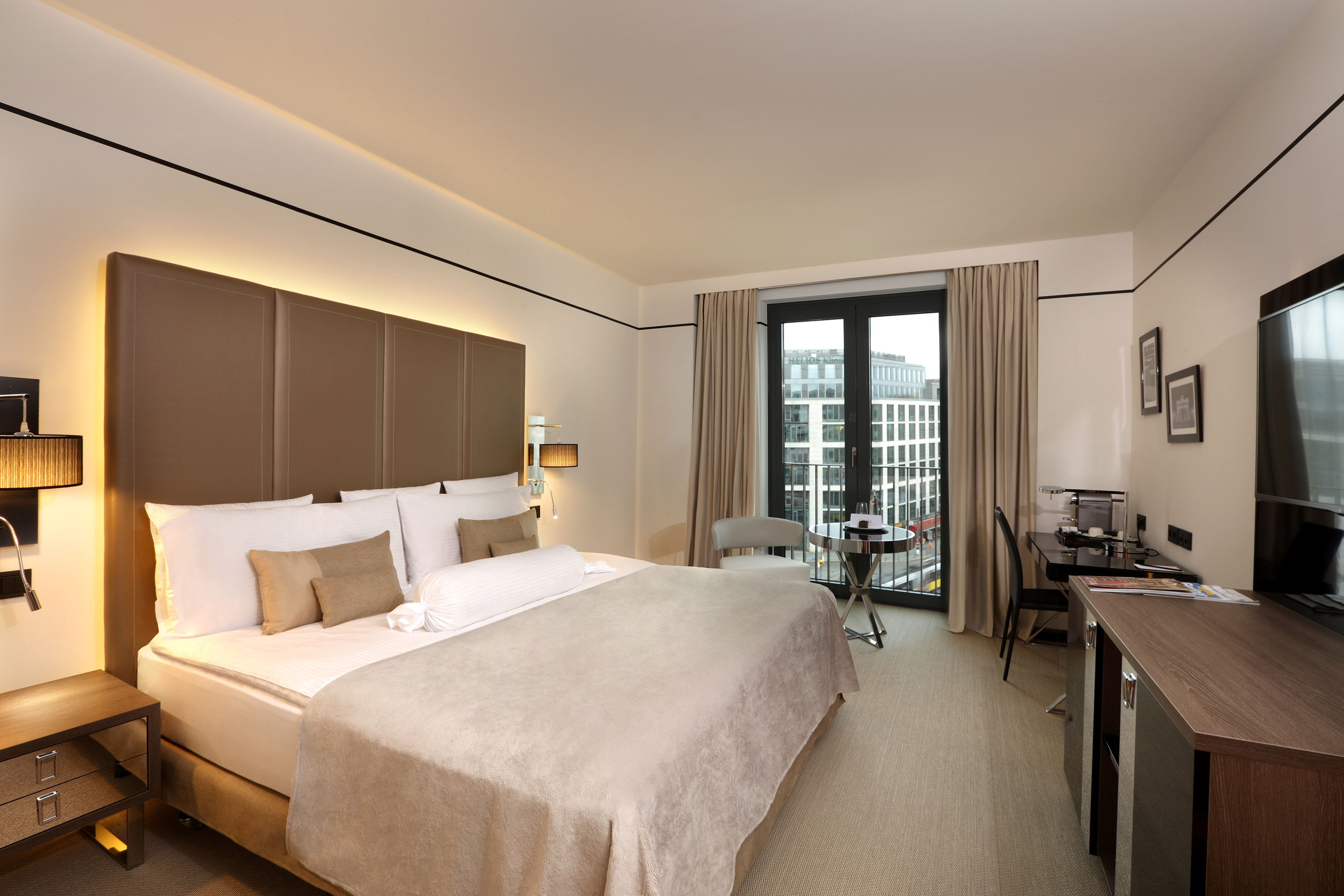 Modern hotel room with king bed, large window city view, and desk area.