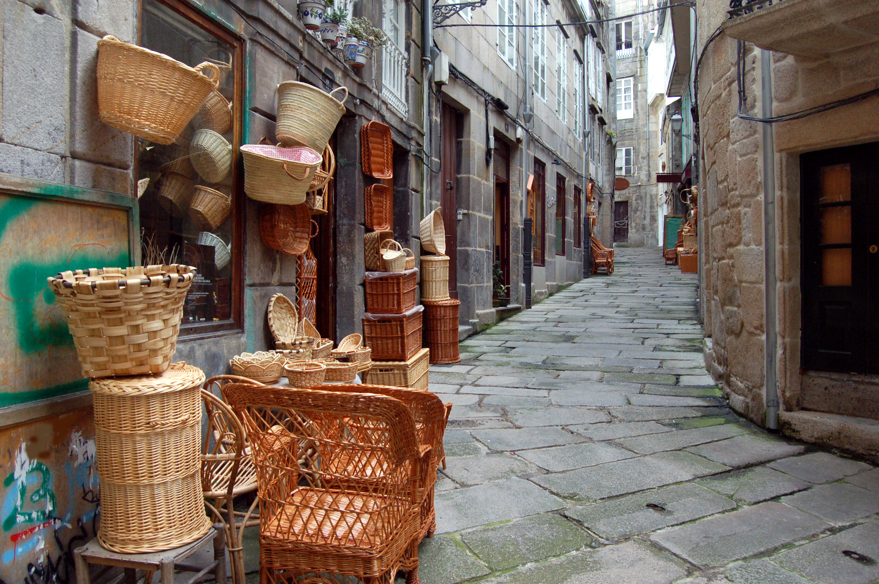 Wicker baskets and furniture display outside a shop on a cobblestone alley.