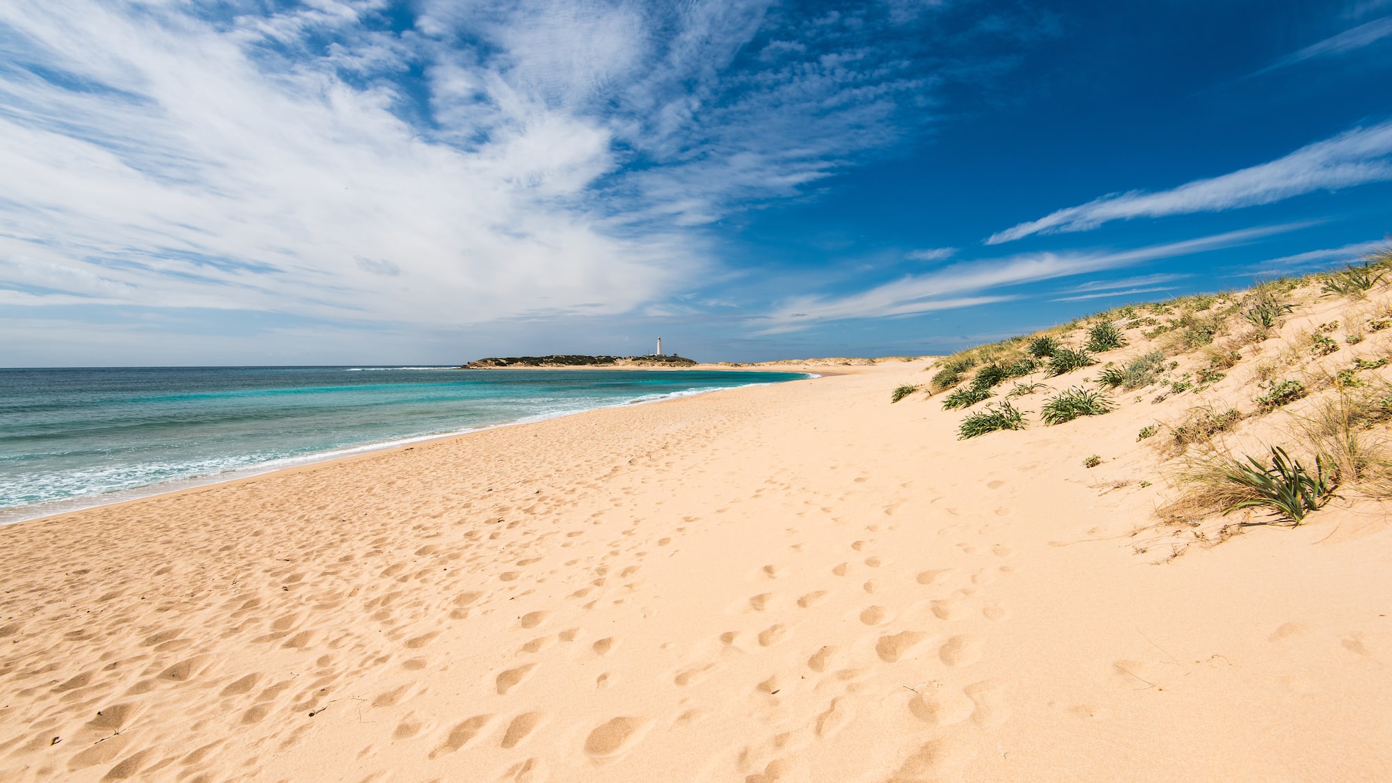a sandy beach with blue water and blue sky