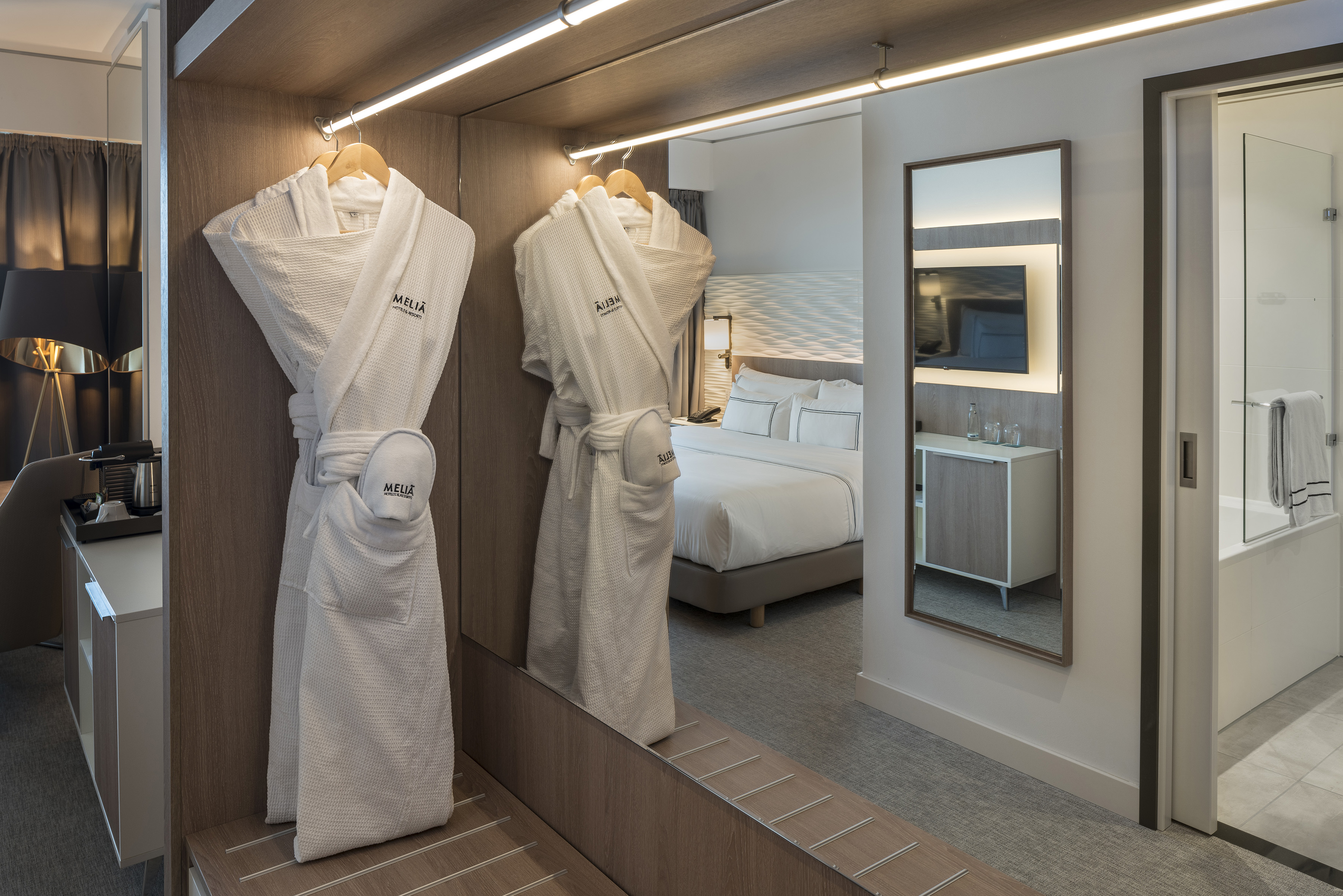 Modern Meliá hotel room with bathrobes, mirror shows bedroom and bathroom.