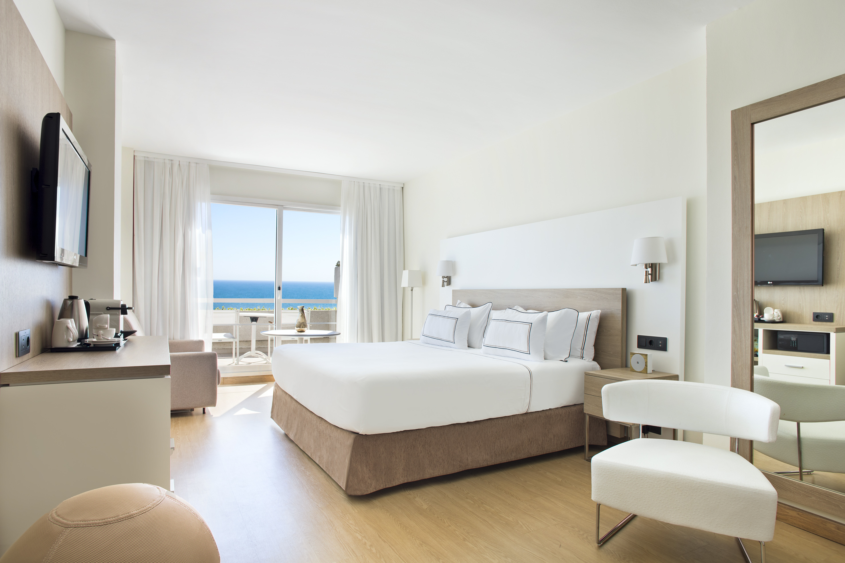 Modern hotel bedroom with king bed, ocean view balcony, and bright decor.