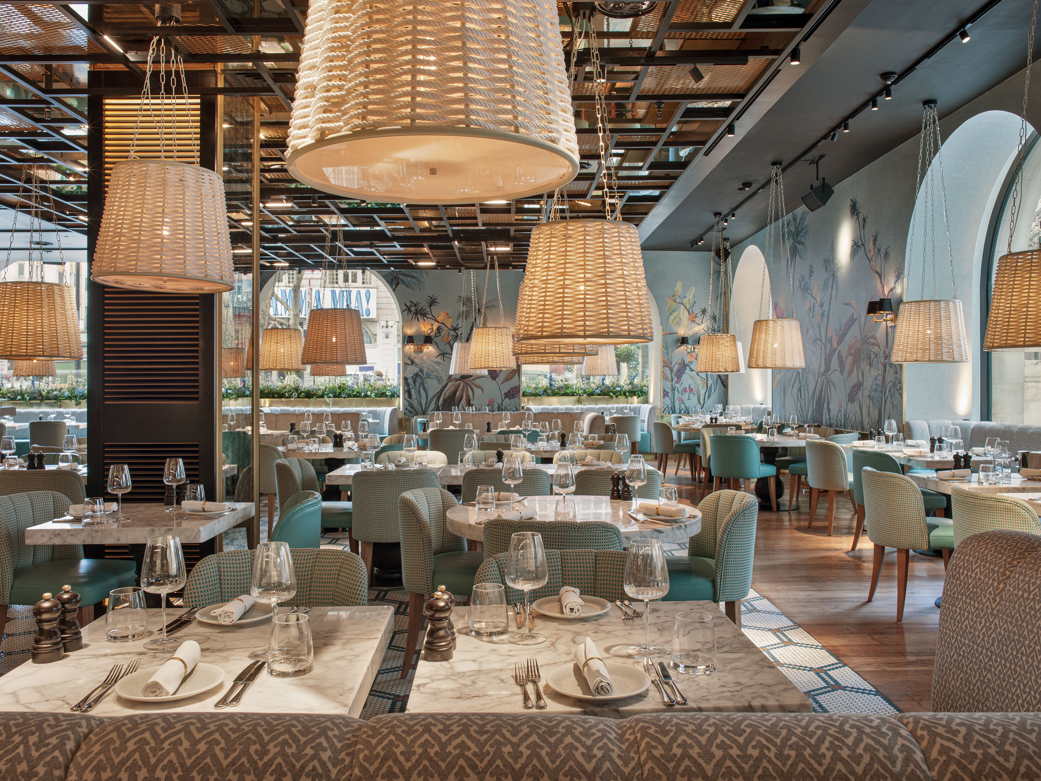 Restaurant dining room with wicker lamps, marble tables, teal chairs.