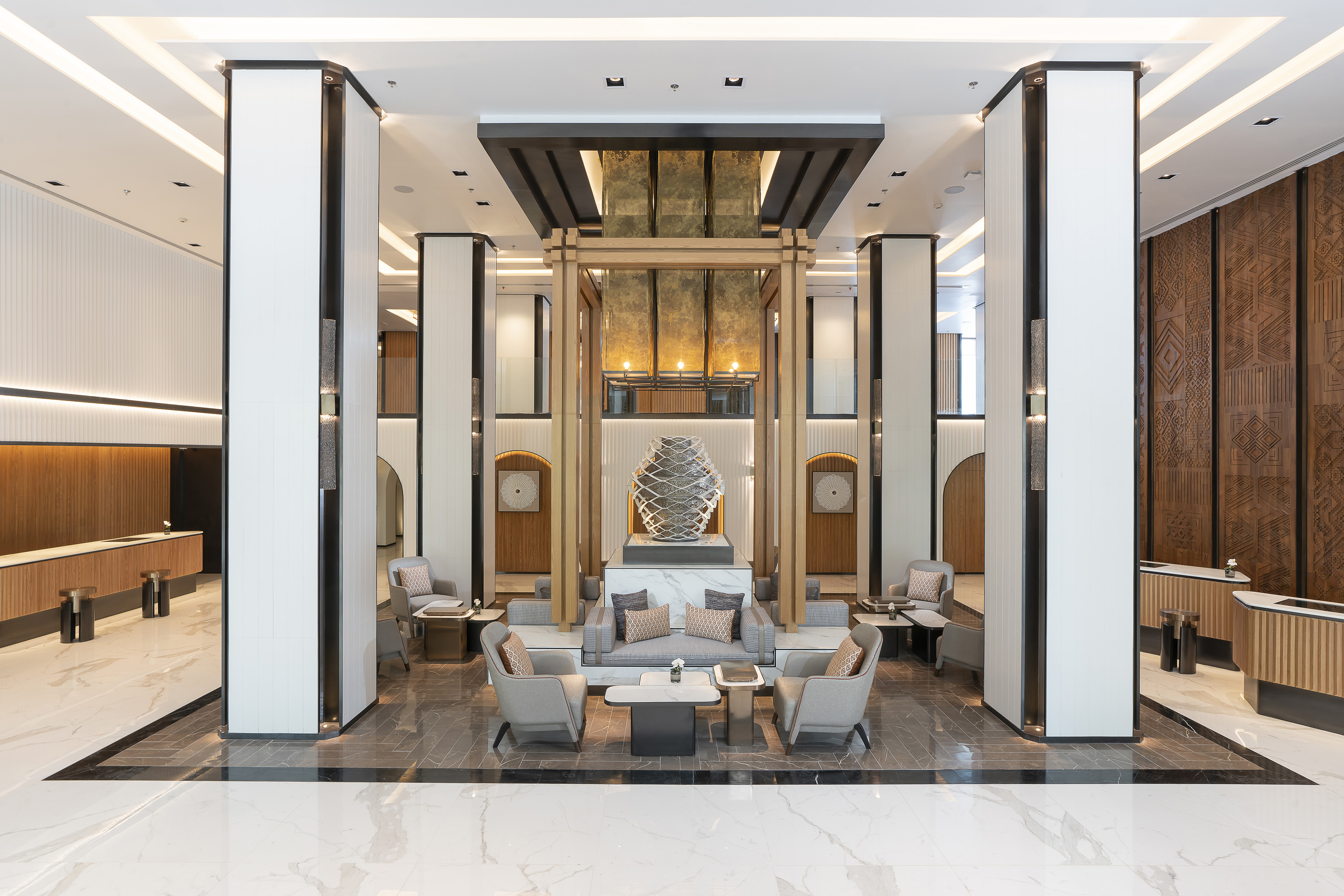 Luxury hotel lobby with modern seating, central art piece, and decorative wood panels.