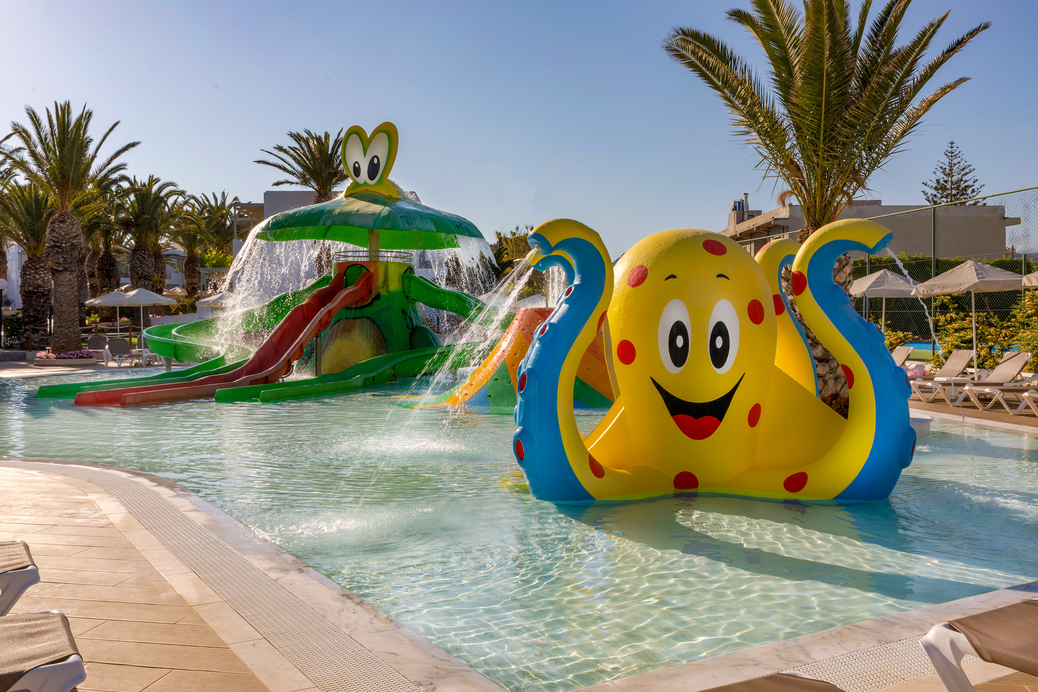 Sunny resort water park with colorful octopus and frog slides.