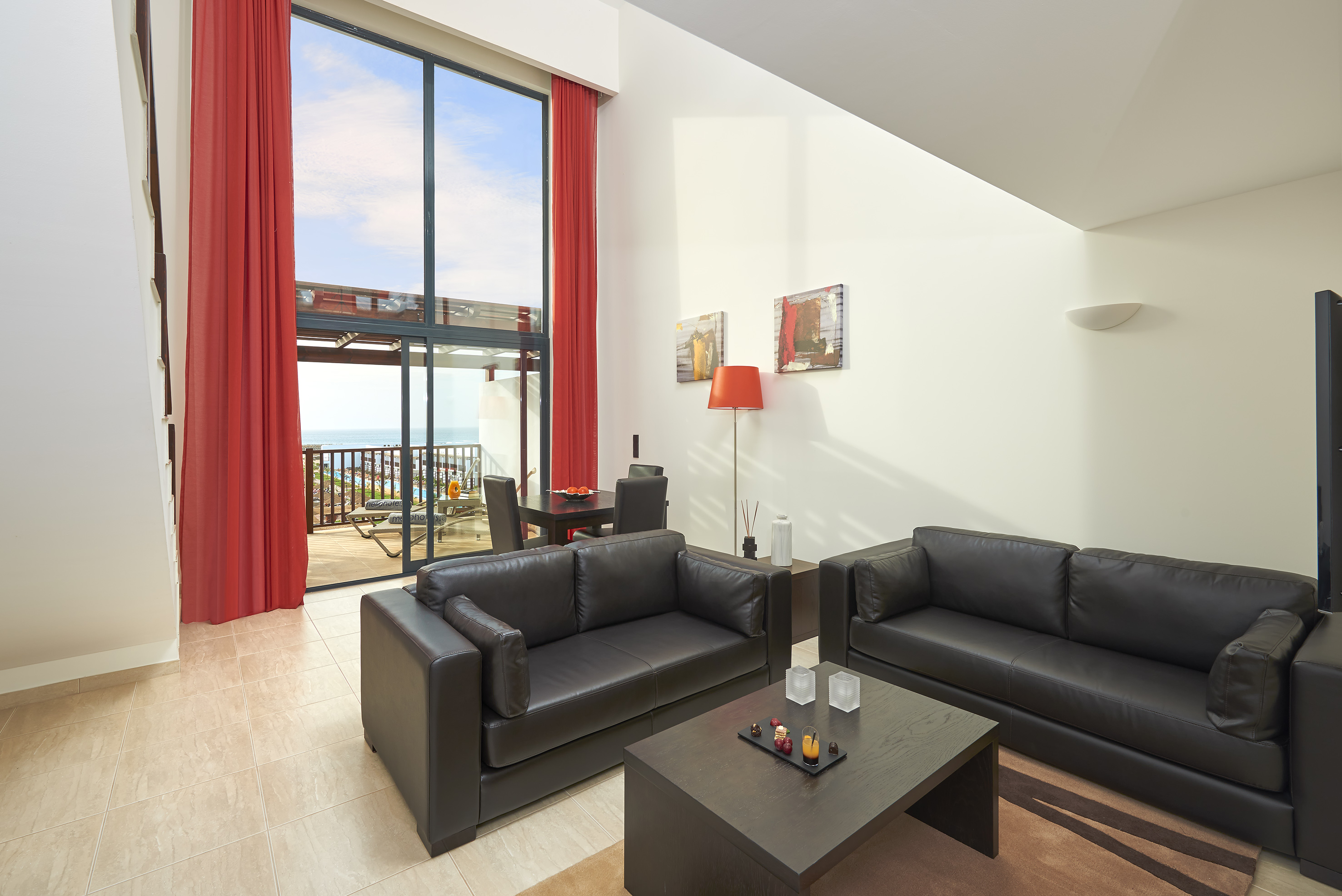 a living room with black couches and red curtains