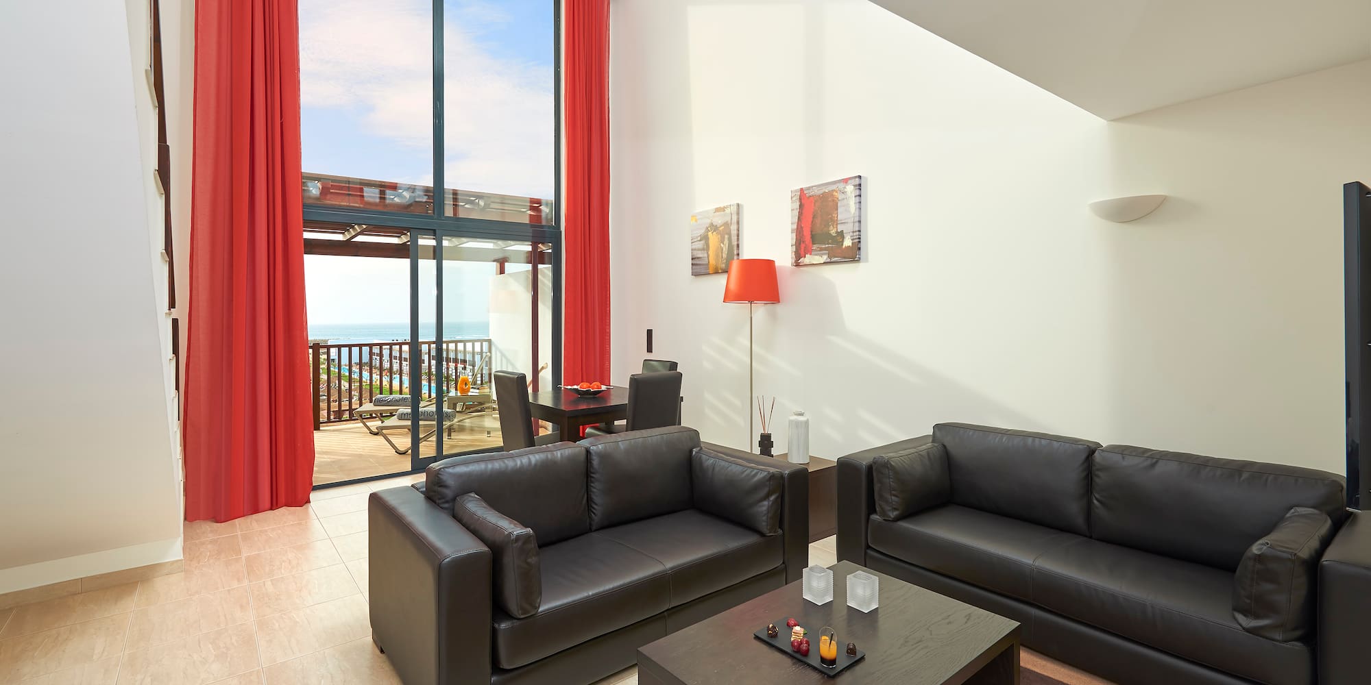 a living room with black couches and red curtains