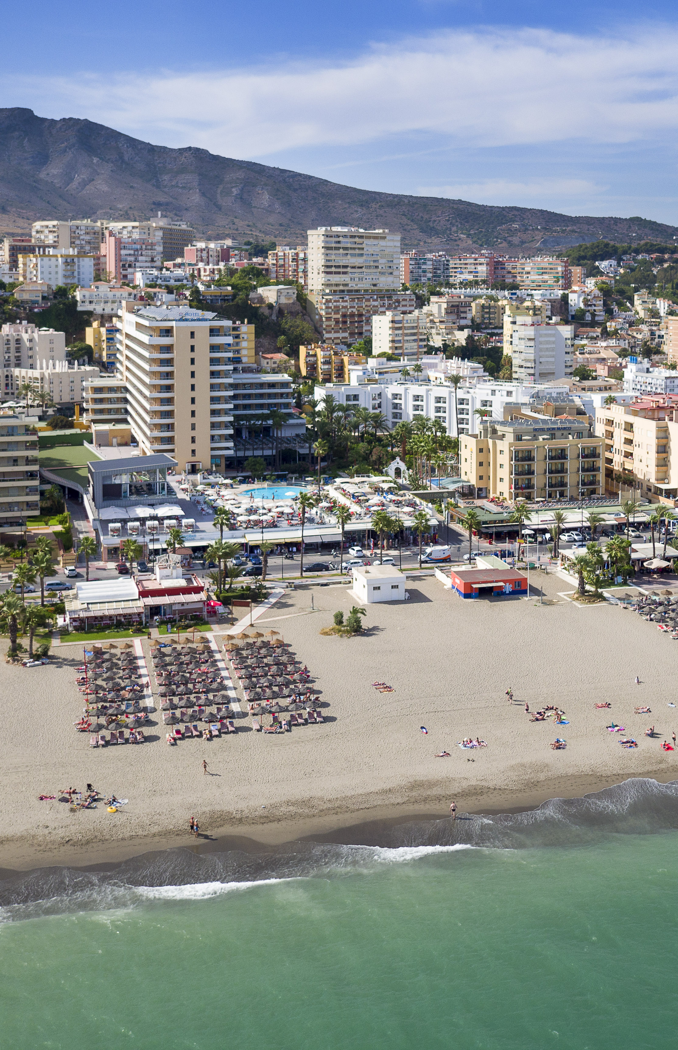 Coastal resort town with sandy beach, ocean, hotels, and mountain backdrop.
