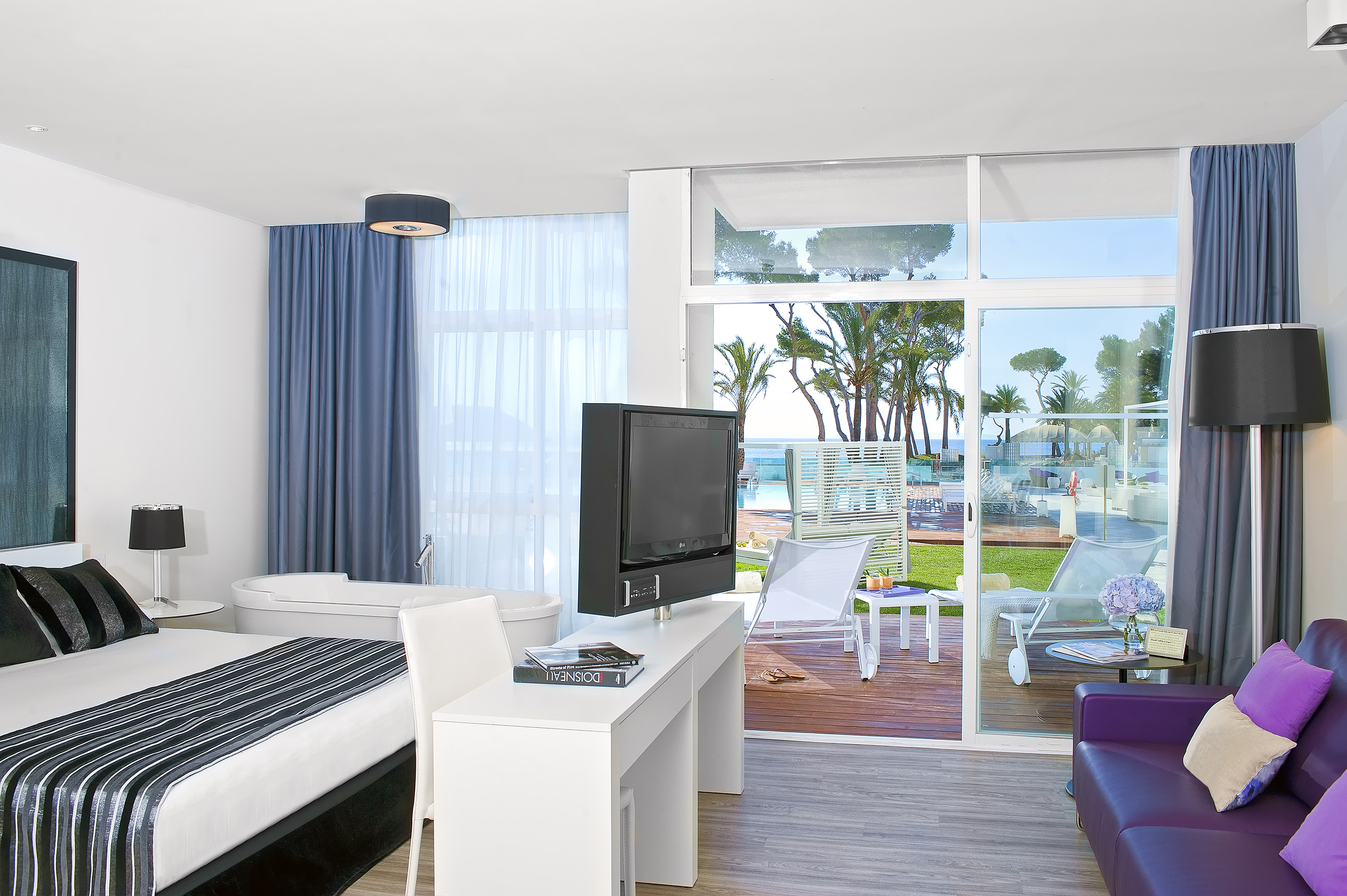 Modern hotel room with ocean and pool view, bed, bath, and patio.