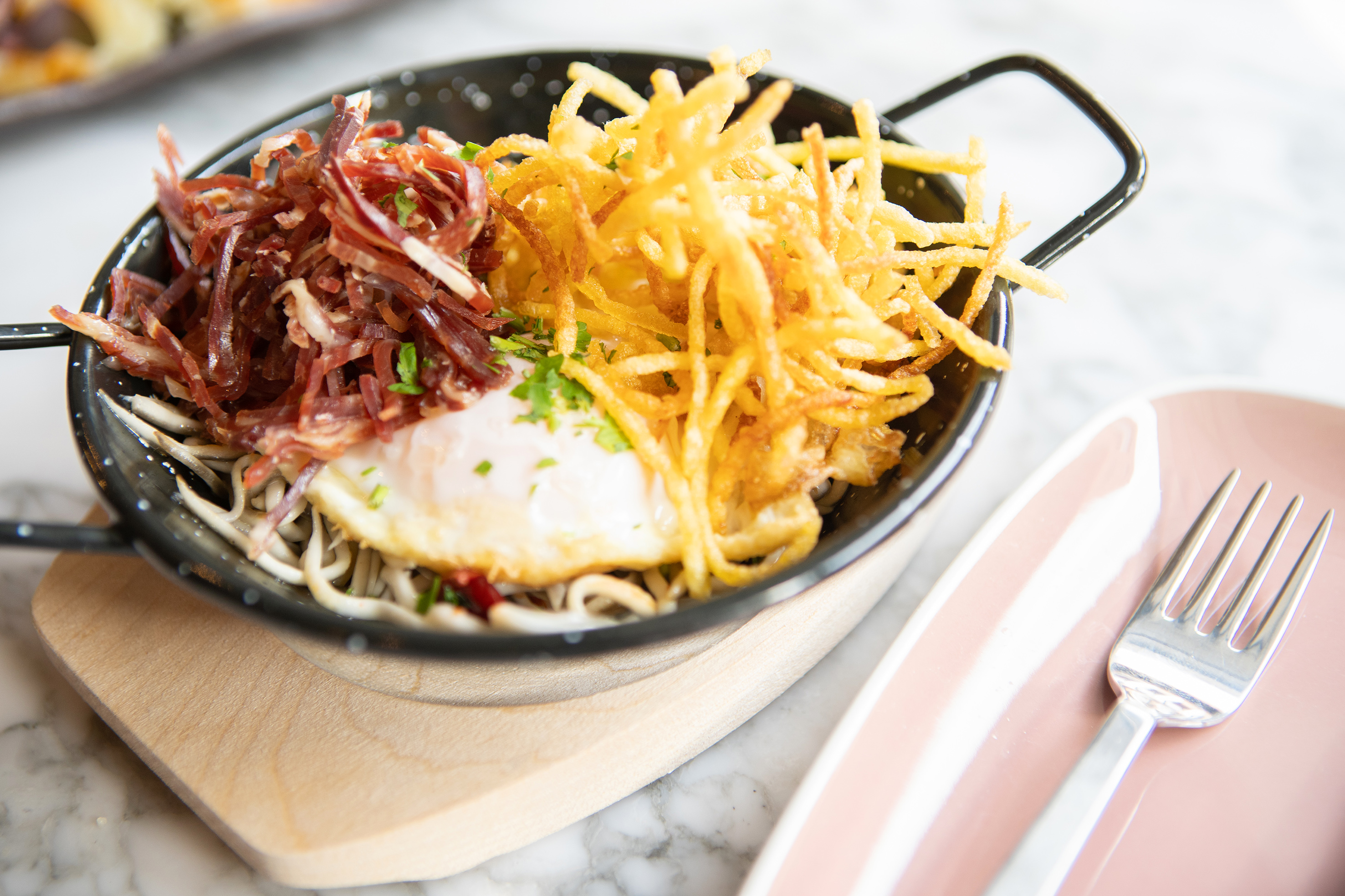 Skillet with fried egg, shredded jamón, and crispy straw potatoes.