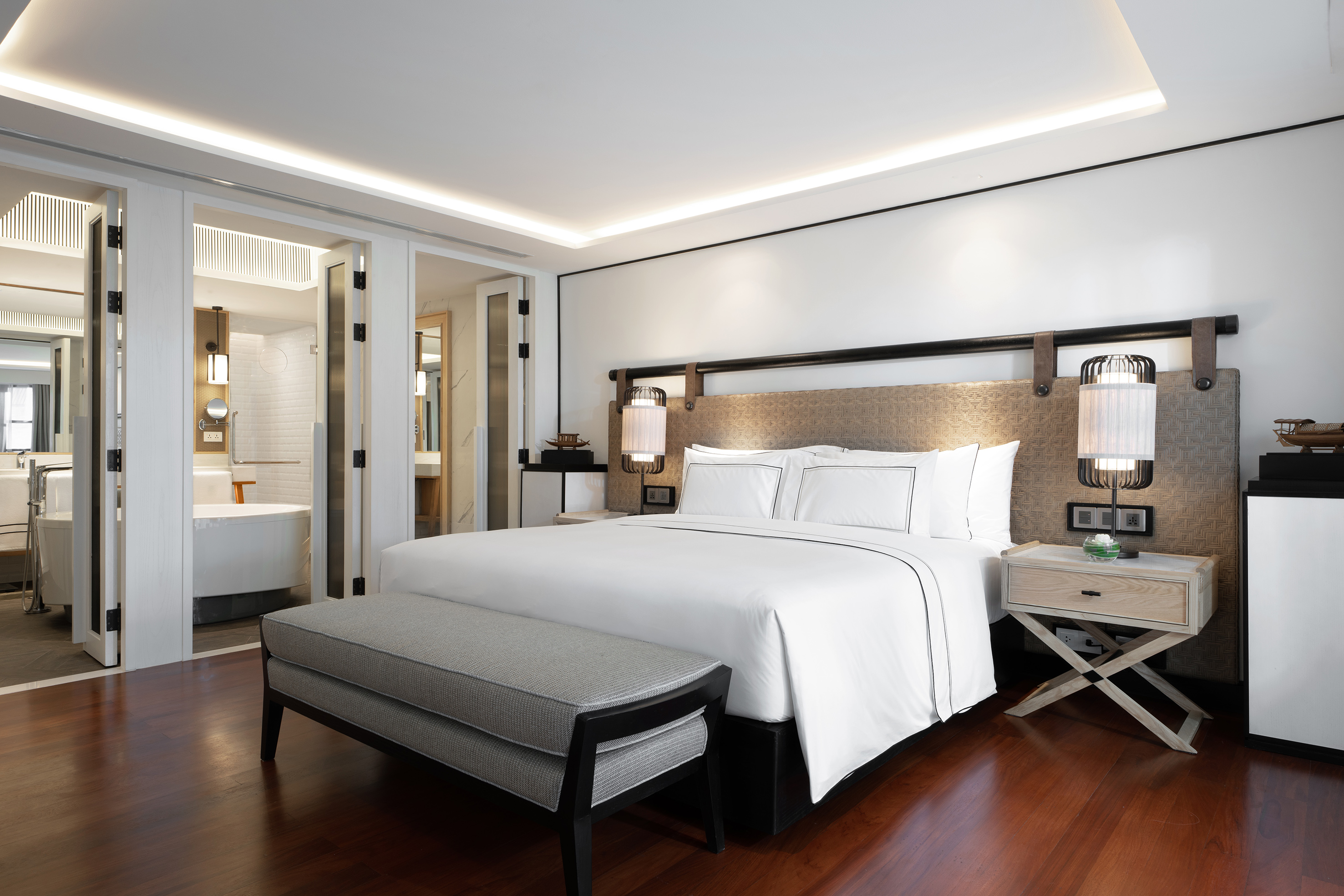 Luxury hotel bedroom with white bed, modern lamps, and visible ensuite bathroom.