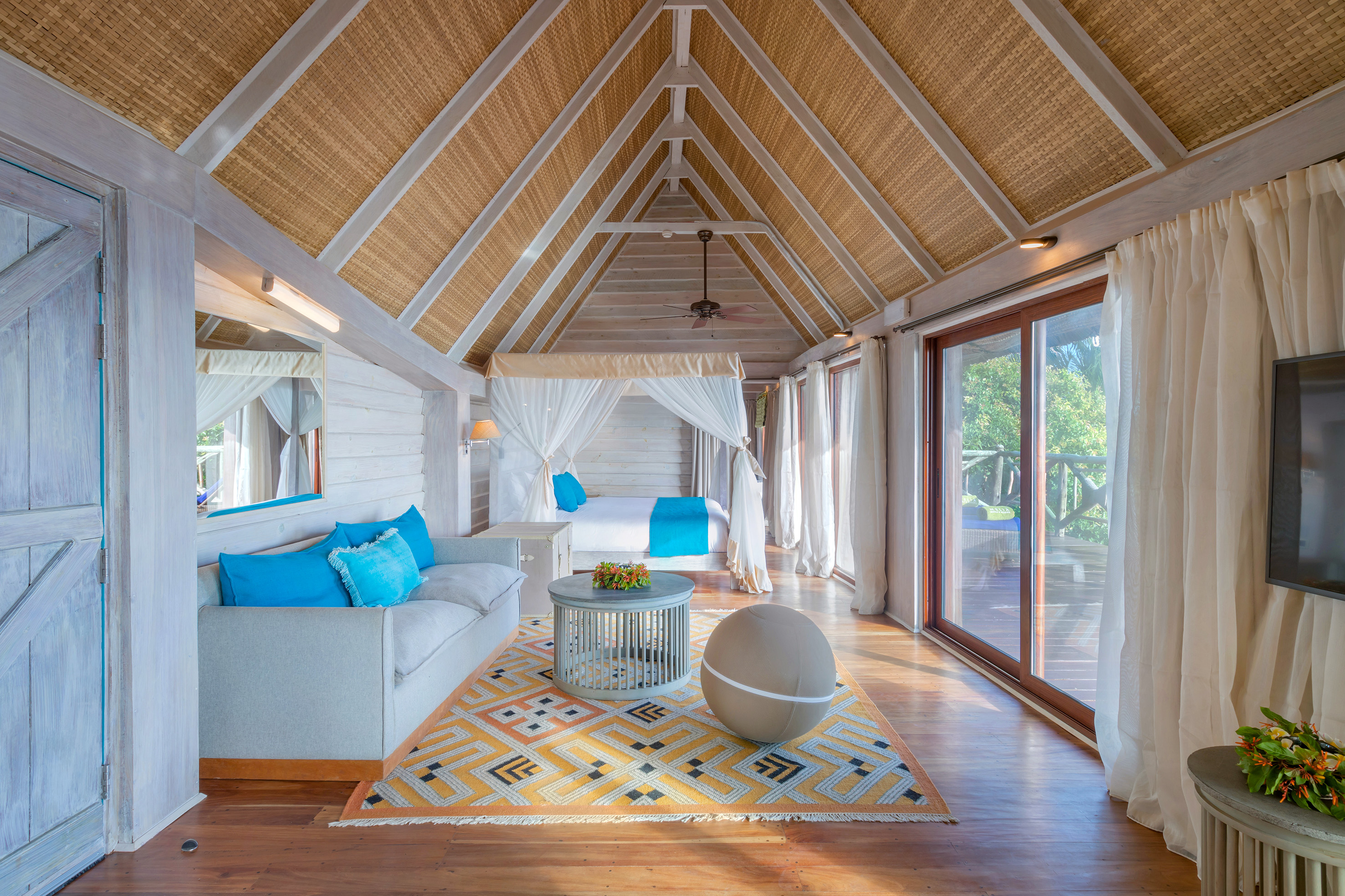 Tropical resort suite with canopy bed, woven ceiling, and balcony.