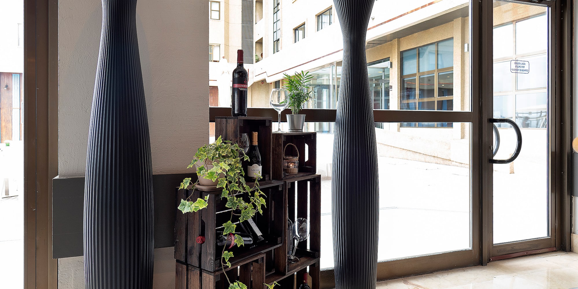 a wine rack with plants and a tall vase in front of a glass door
