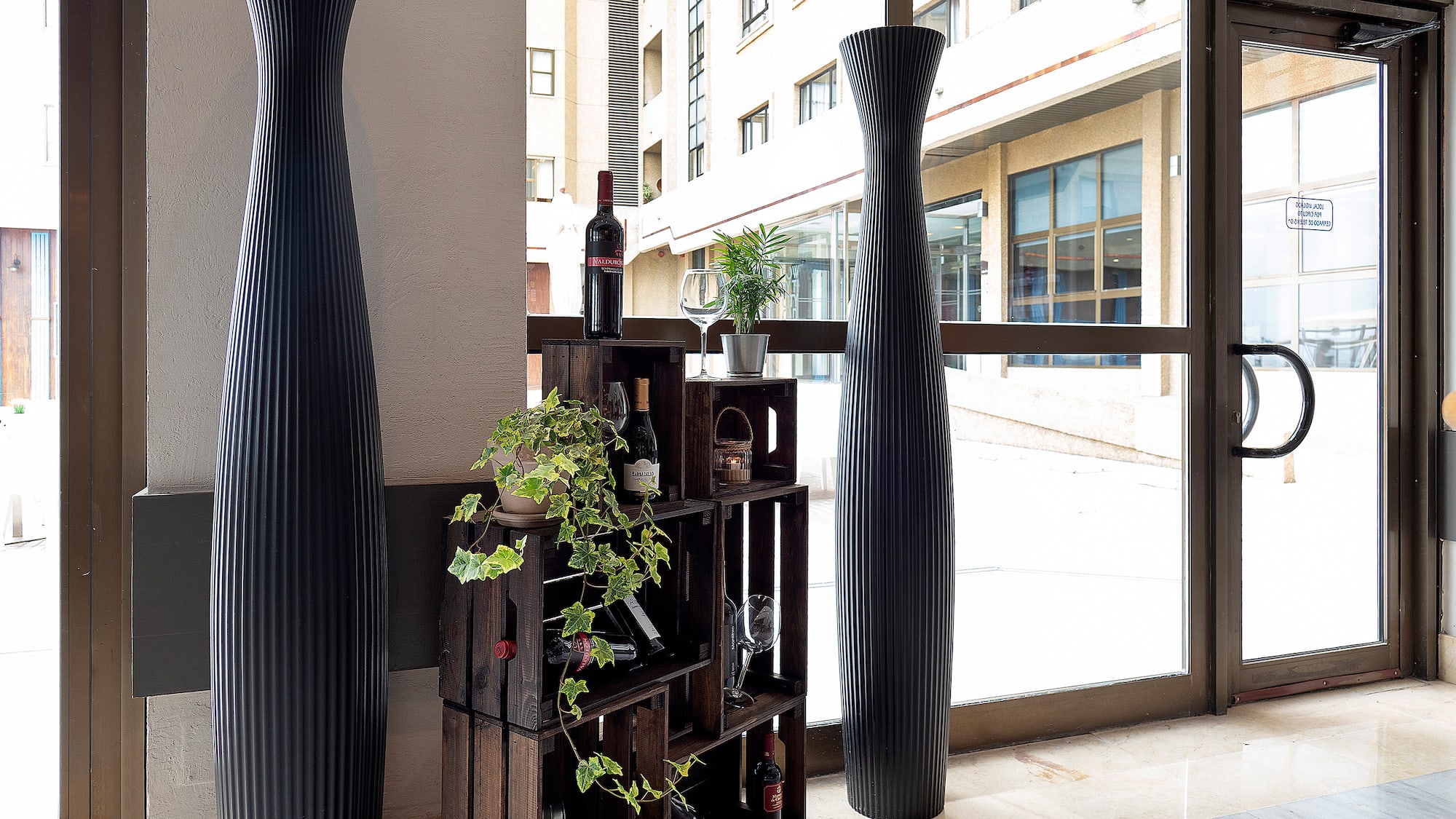 a wine rack with plants and a tall vase in front of a glass door