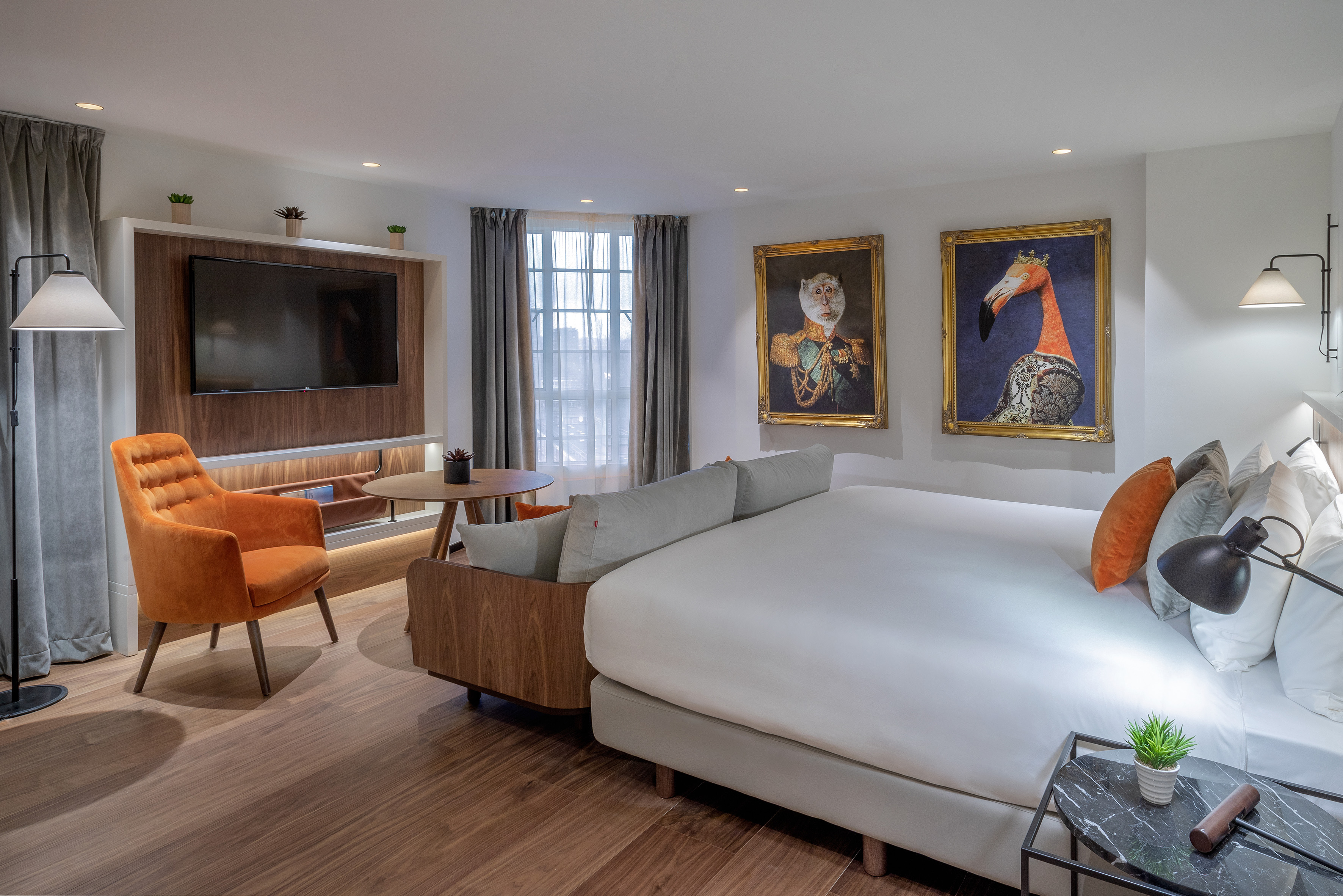 Stylish hotel room with bed, lounge area, TV, and framed animal portraits.