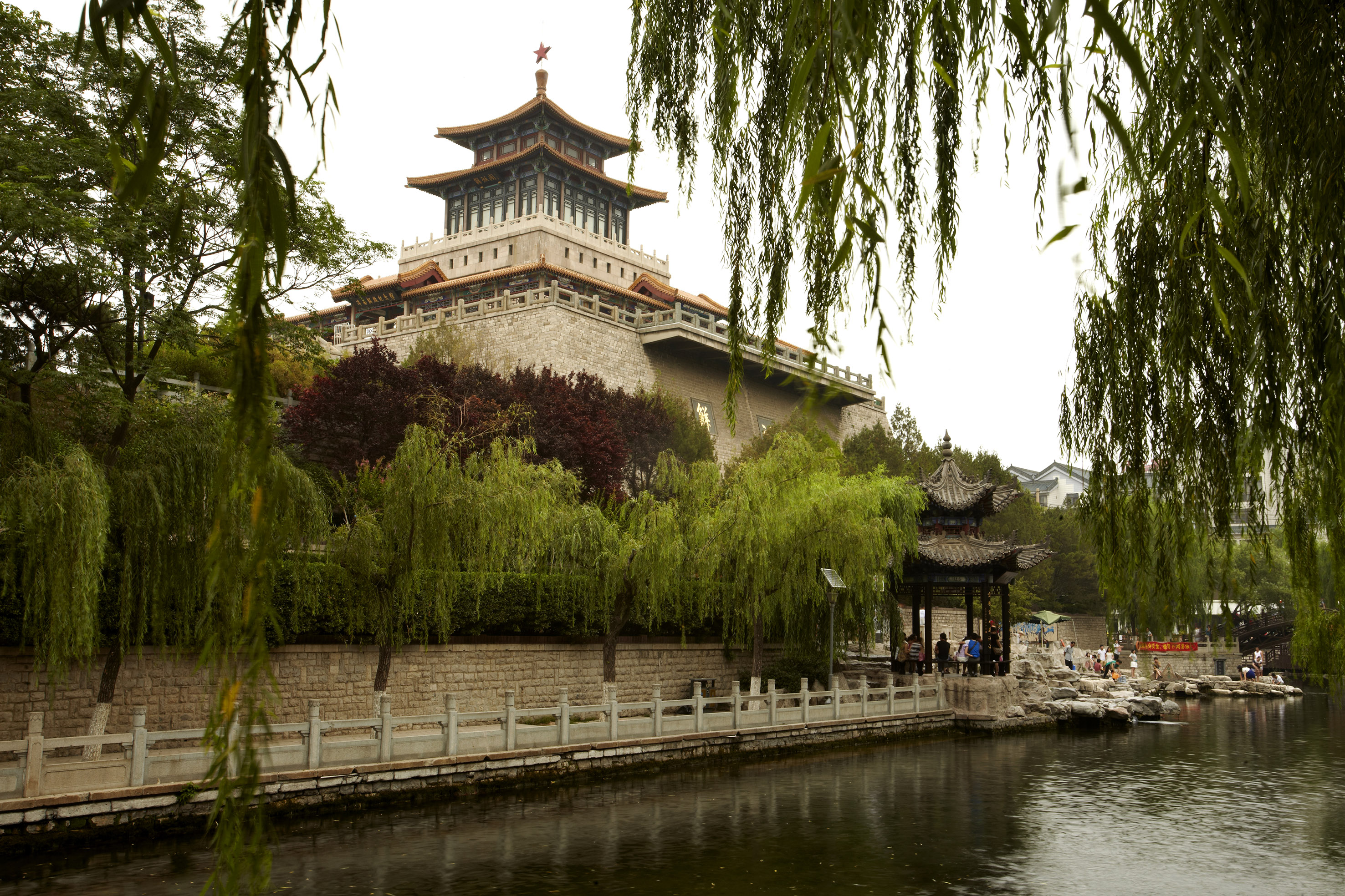 Traditional Chinese tower with red star by water, framed by weeping willows.