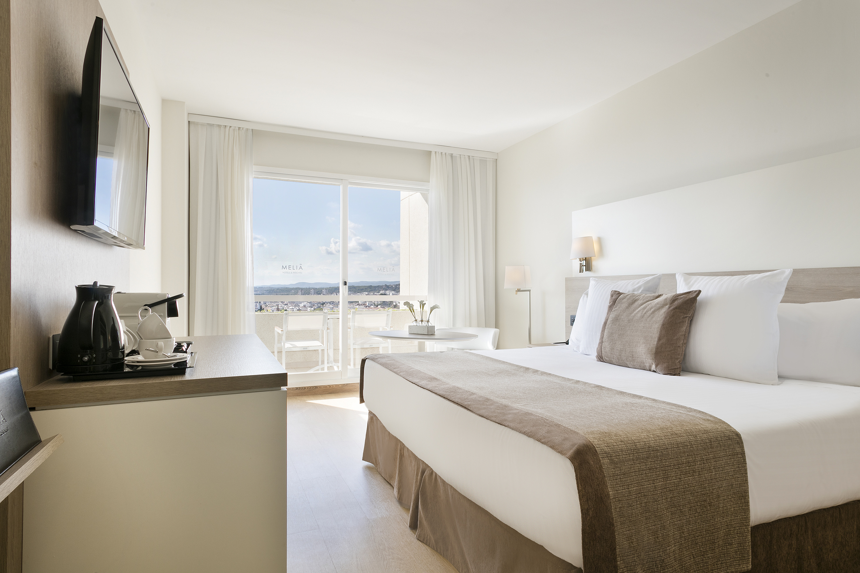 Modern Meliá hotel room with bed, balcony city view, and coffee station.