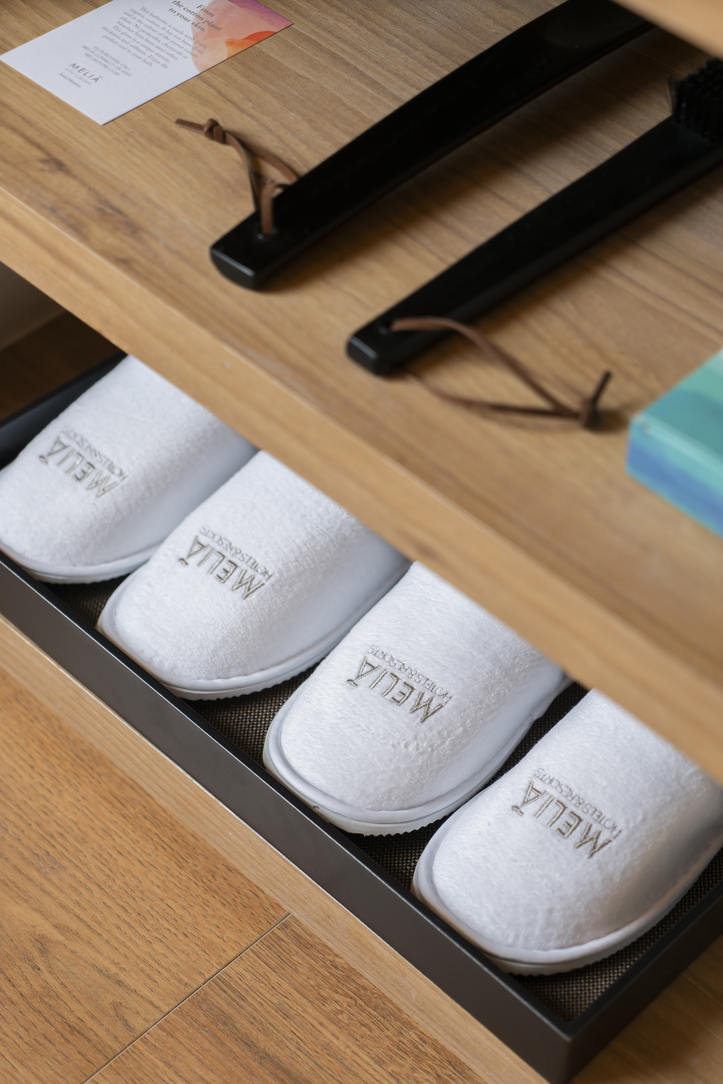 White Melia Hotels & Resorts slippers on a wooden shelf, hotel amenity.