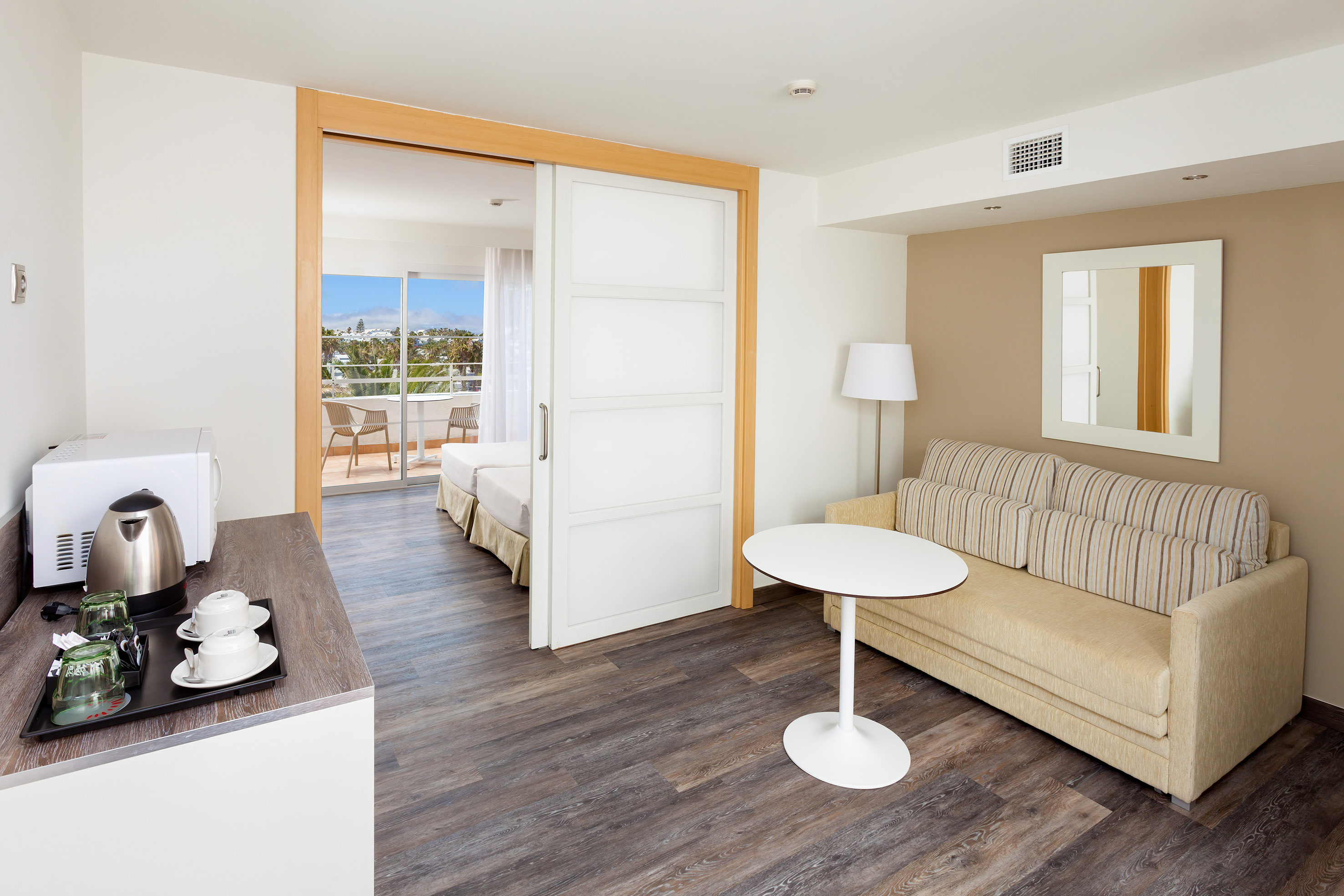 Hotel suite with kitchenette, sofa, twin beds, and balcony view.