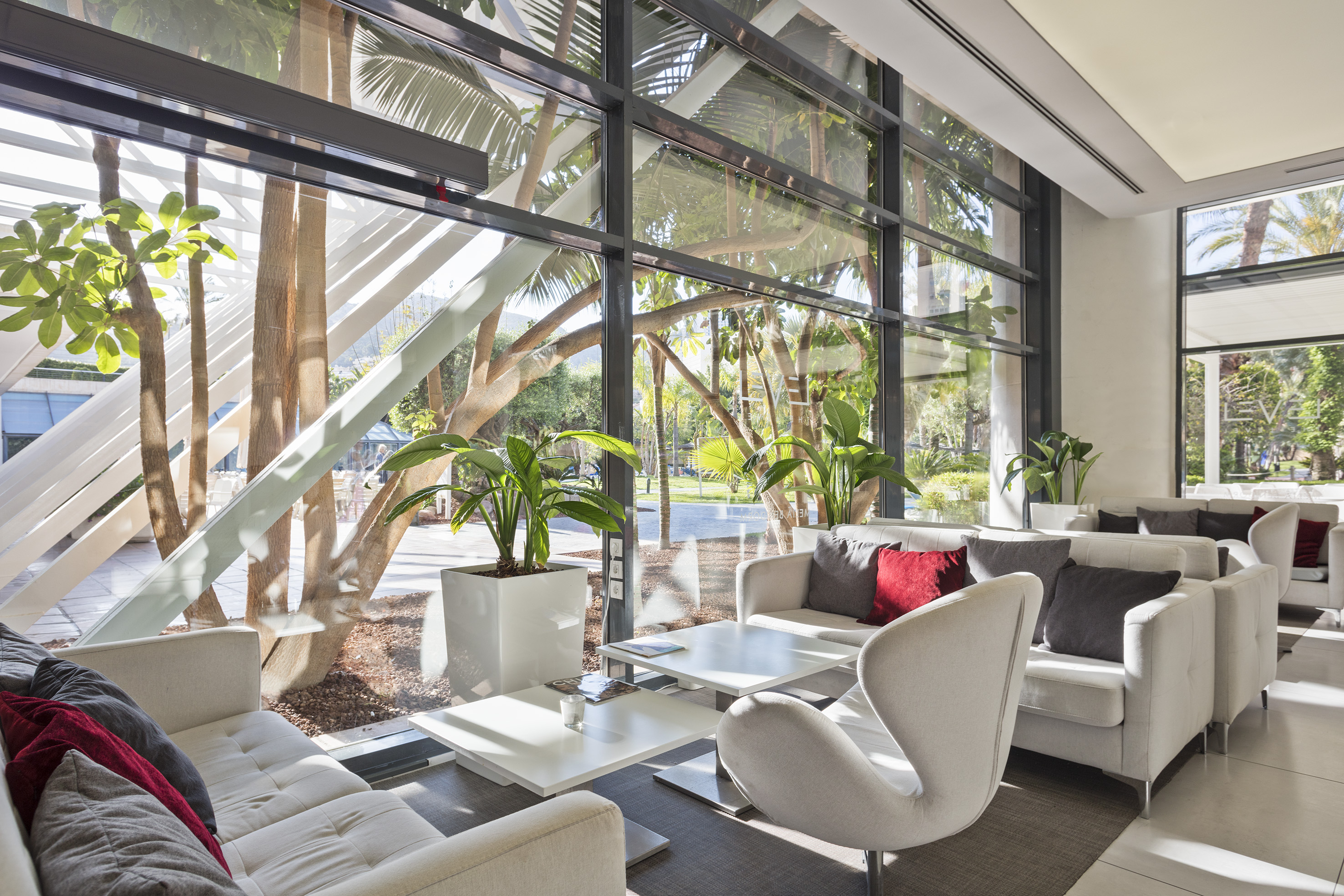 Modern lounge with white sofas, large windows, and tropical garden views.