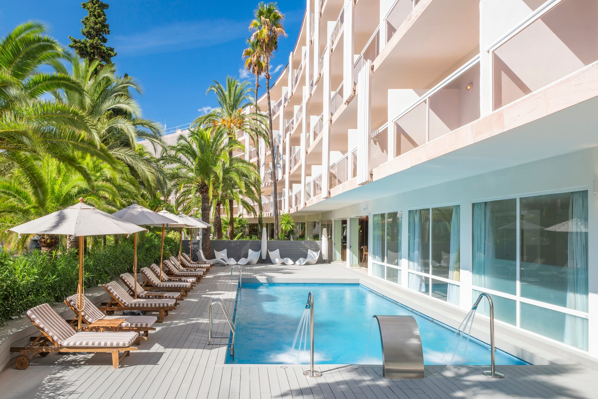 a pool with lounge chairs and umbrellas in front of a building