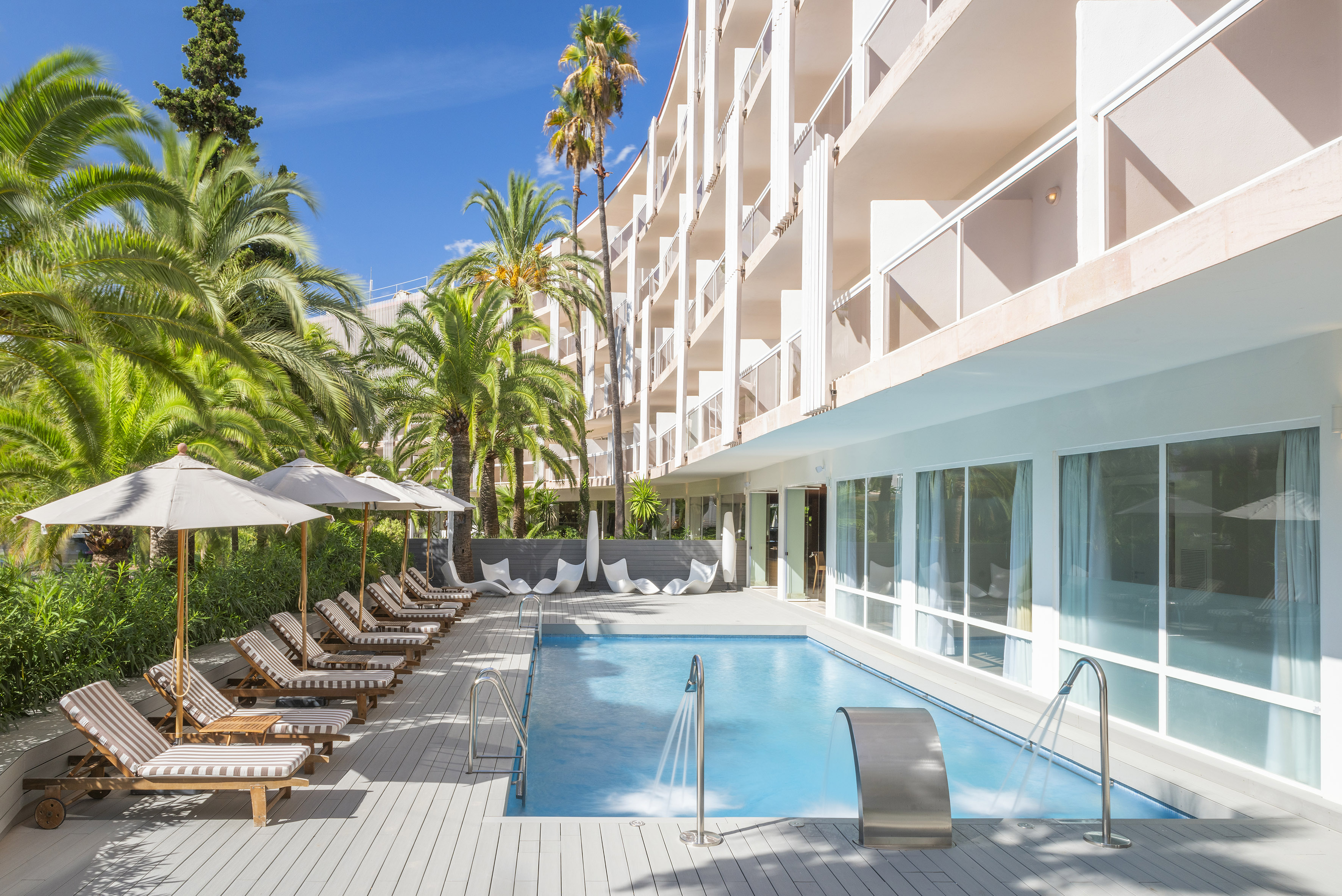 a pool with lounge chairs and umbrellas in front of a building