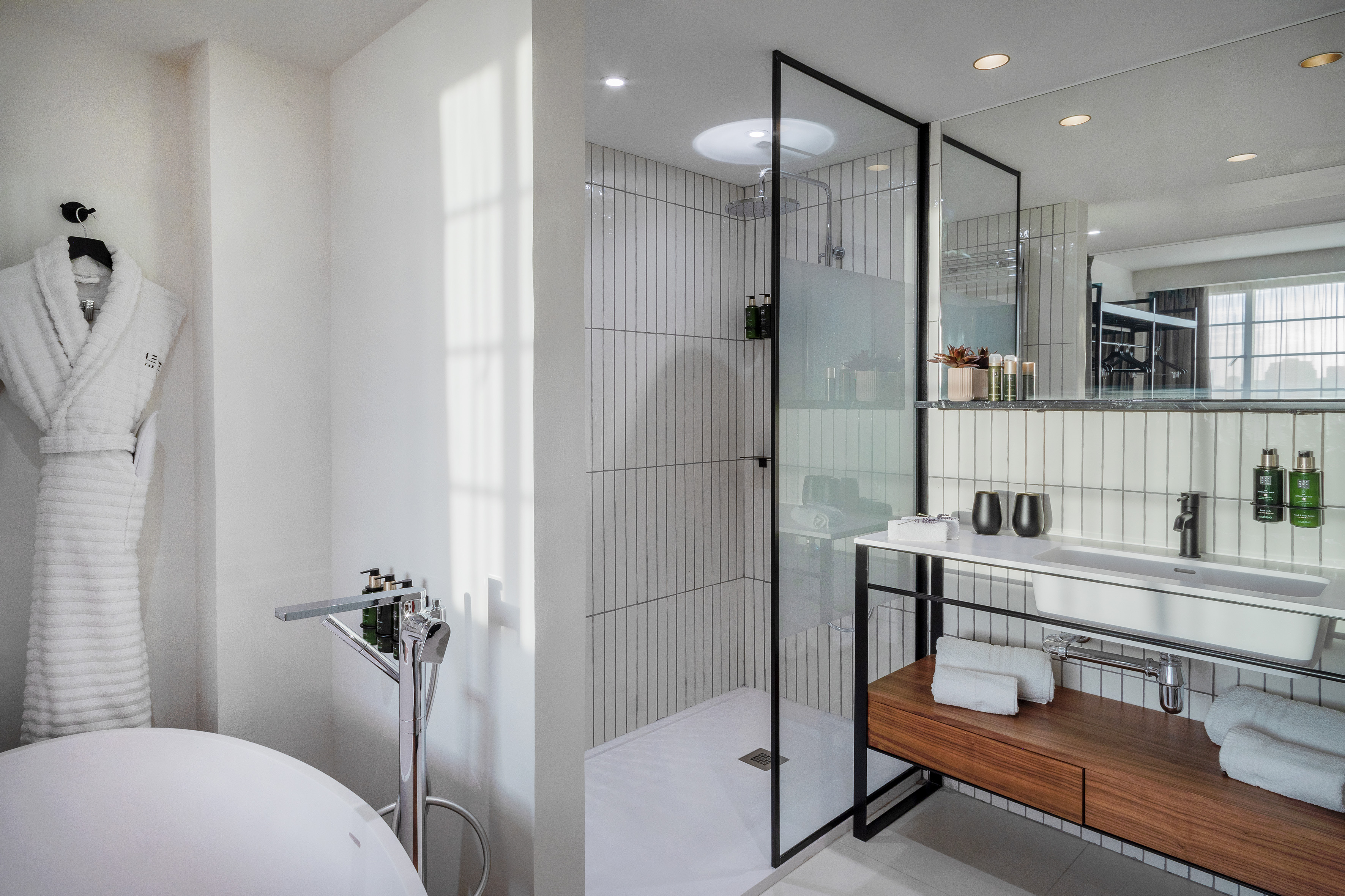 Modern hotel bathroom with white tiles, walk-in shower, freestanding tub, and vanity.