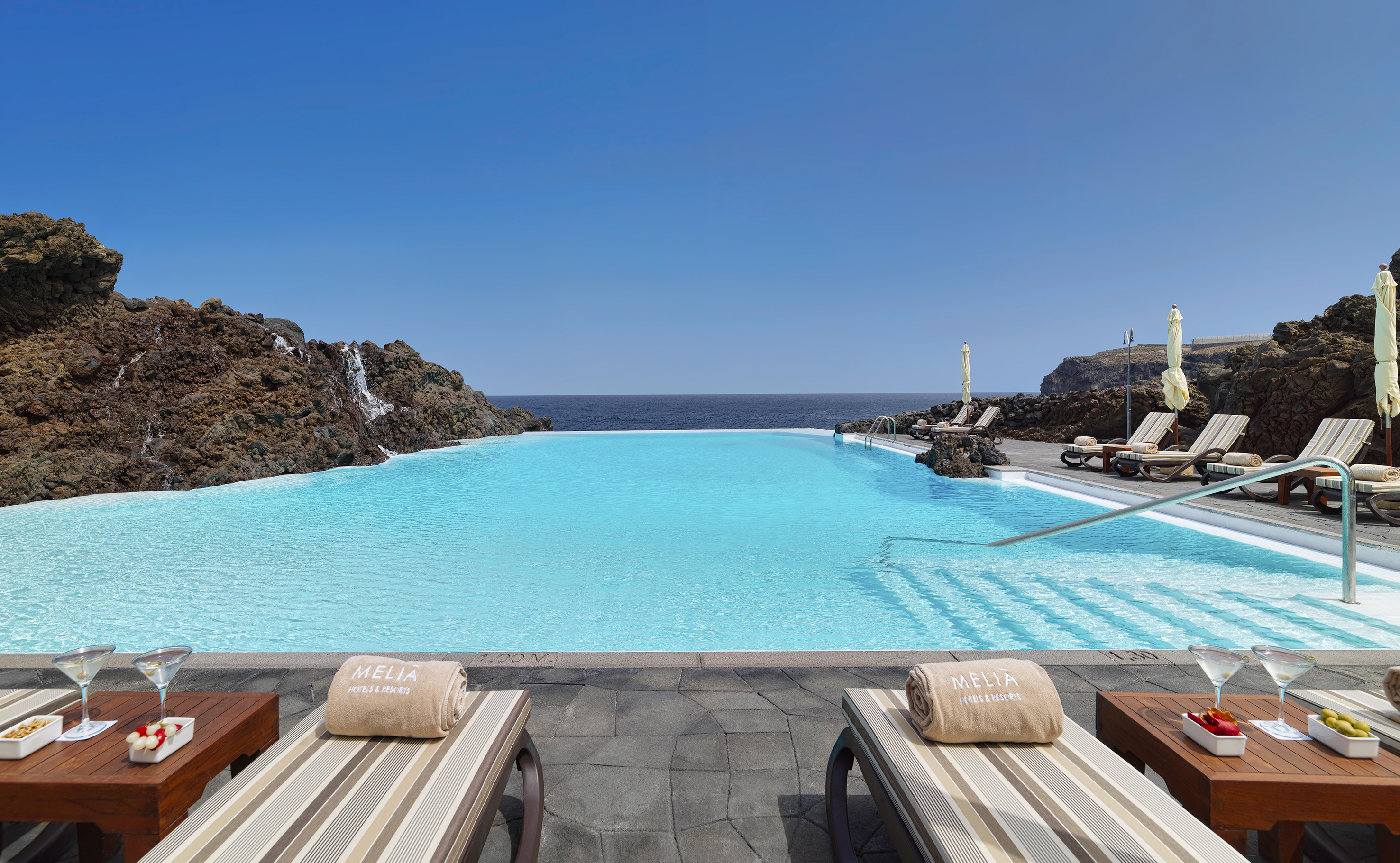 a pool with chairs and rocks in the background