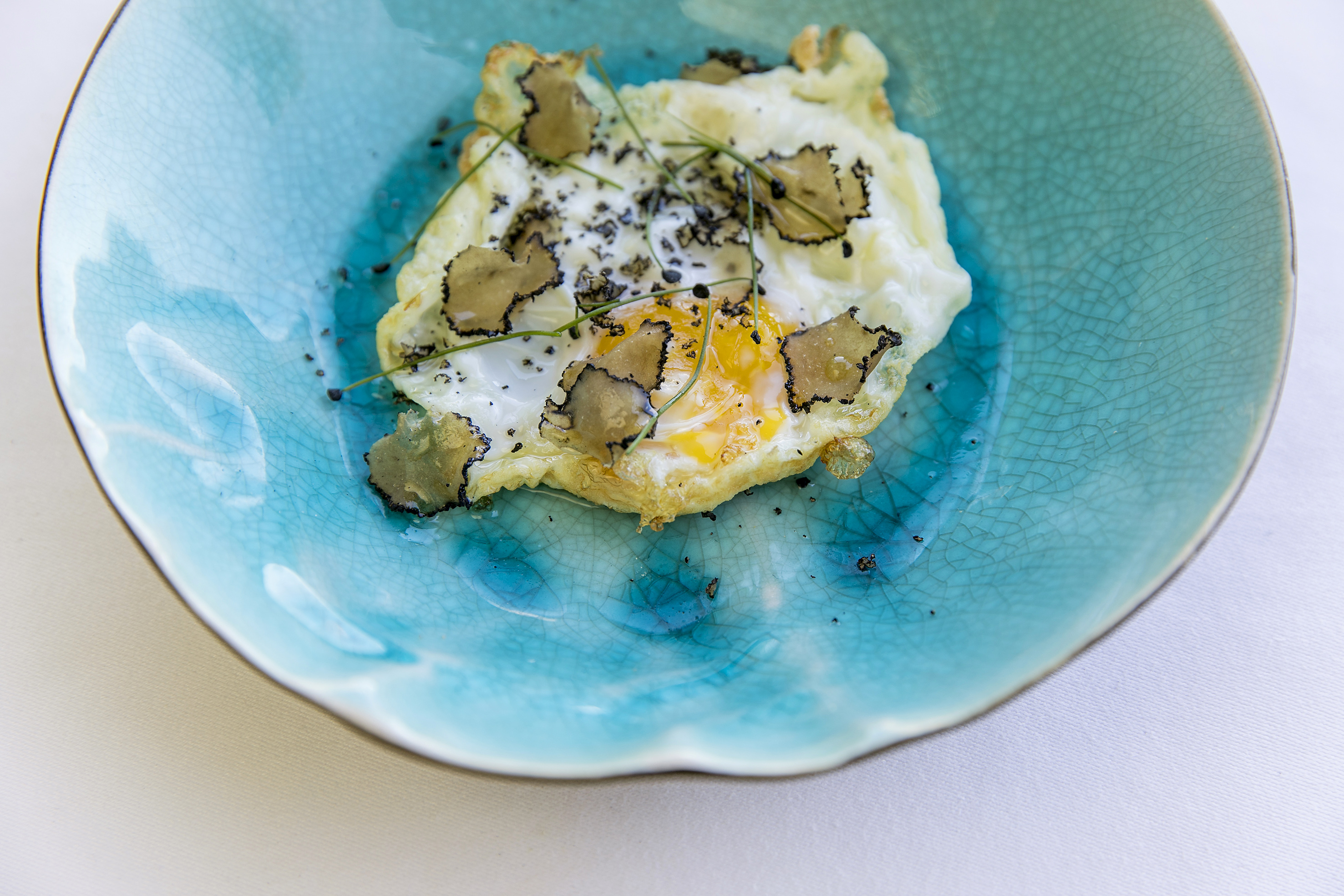 Runny fried egg topped with black truffle shavings and chives in a blue bowl.