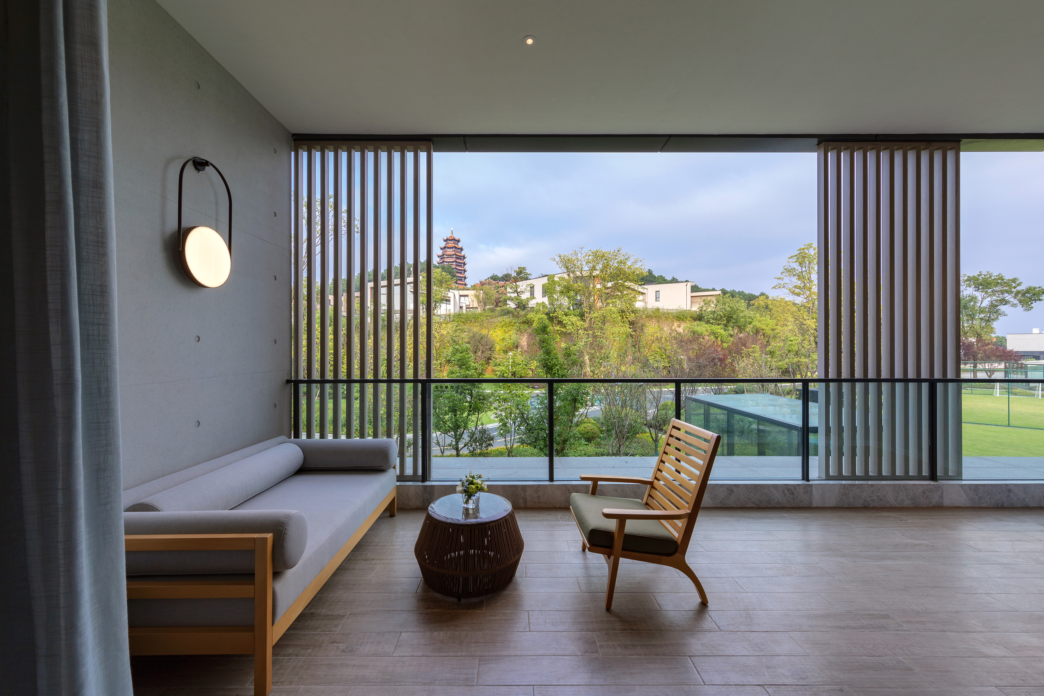 Modern balcony with outdoor seating, hillside view, and traditional pagoda.