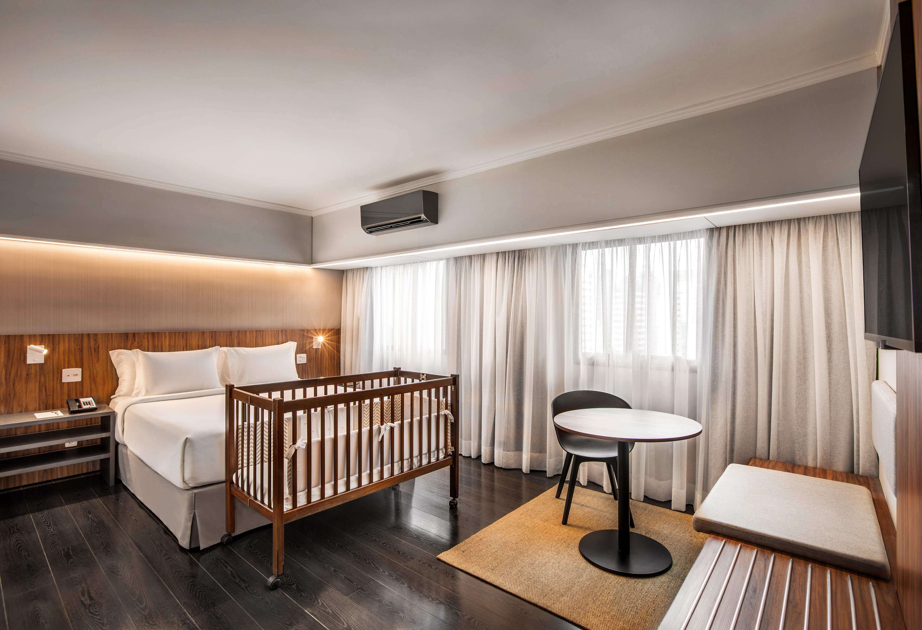Family-friendly hotel room with a comfortable bed and wooden baby crib.
