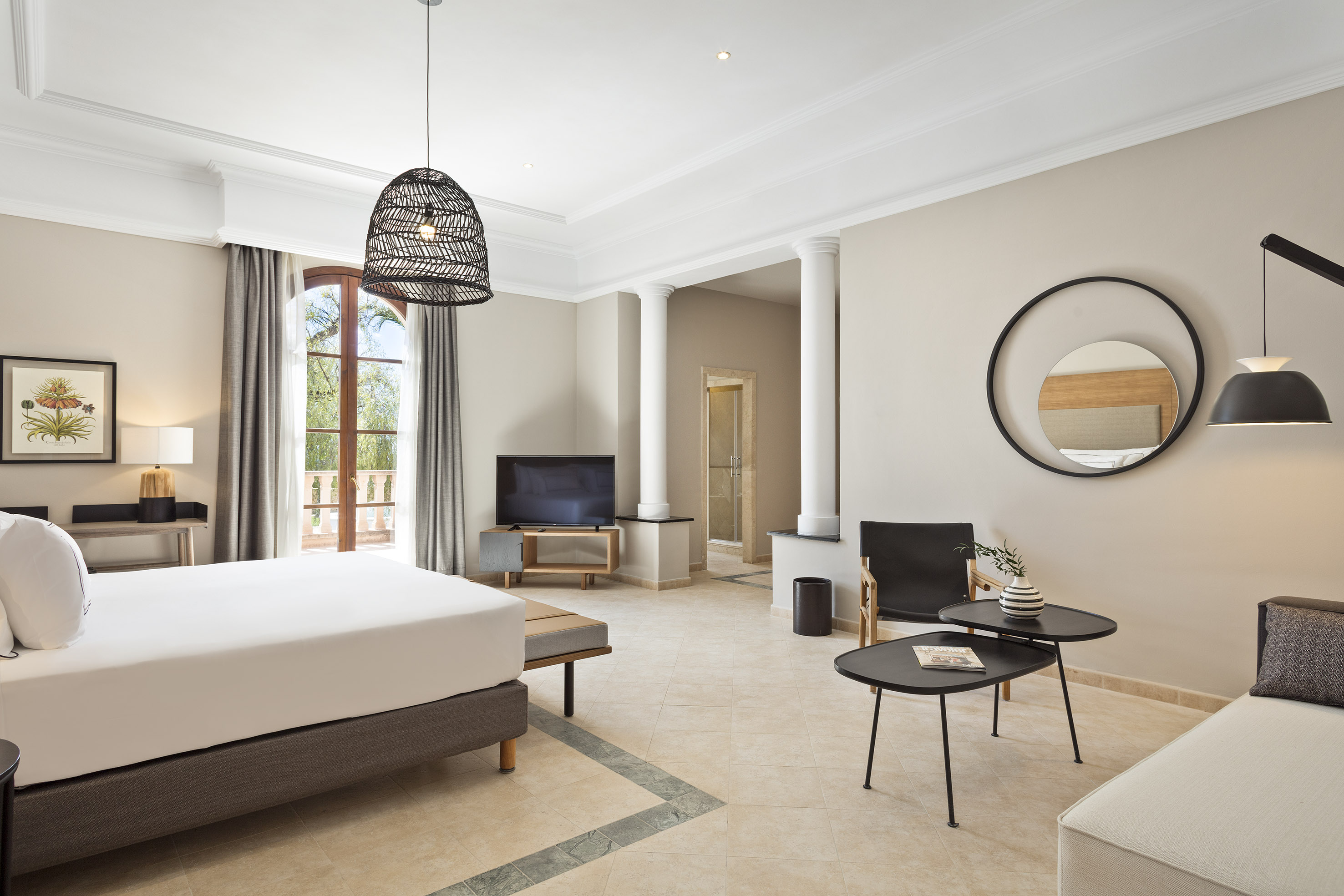 Modern hotel suite with comfortable bed, balcony, seating area, and TV.