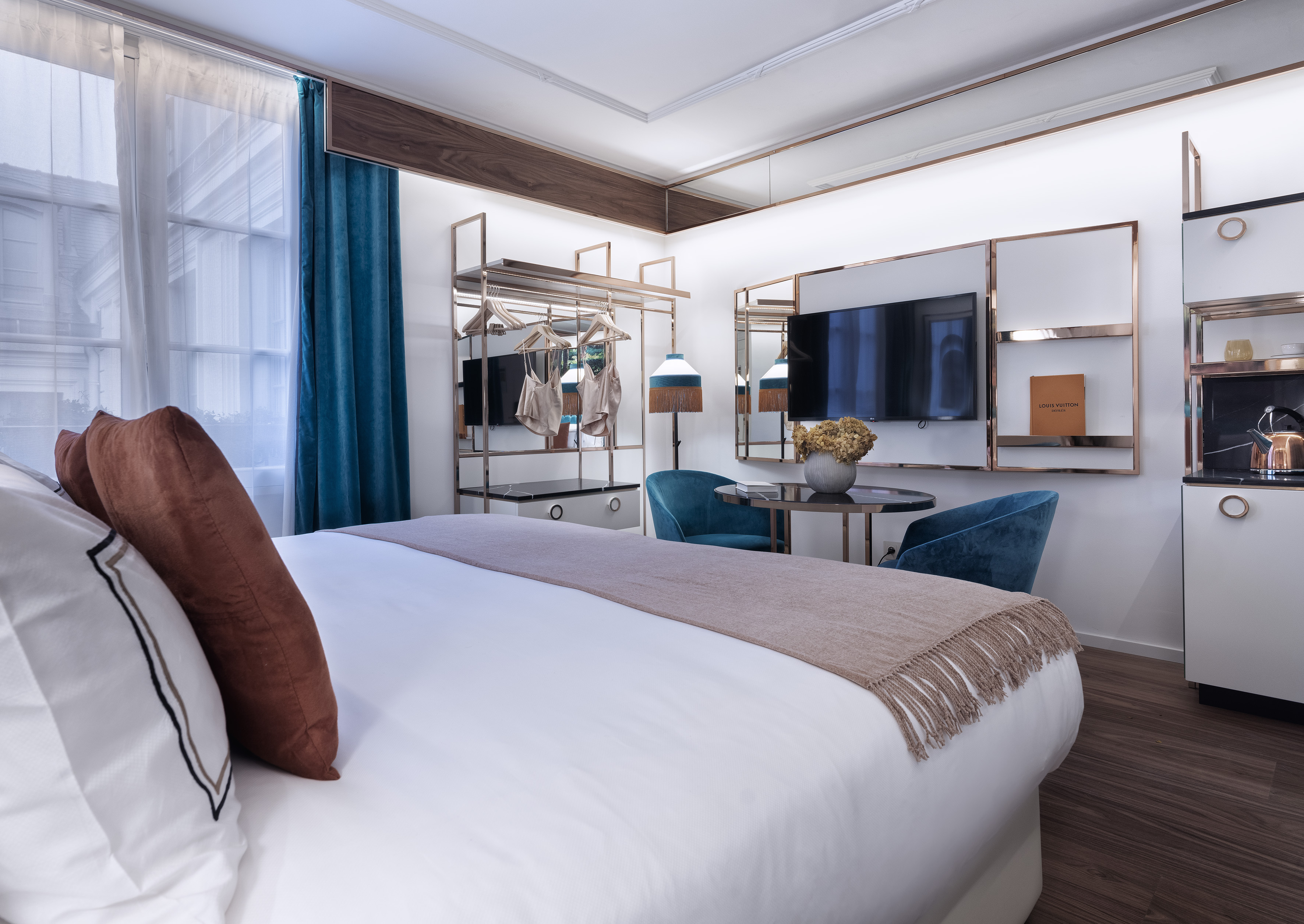 Modern luxury hotel room with bed, teal curtains, wall-mounted TV, and stylish decor.