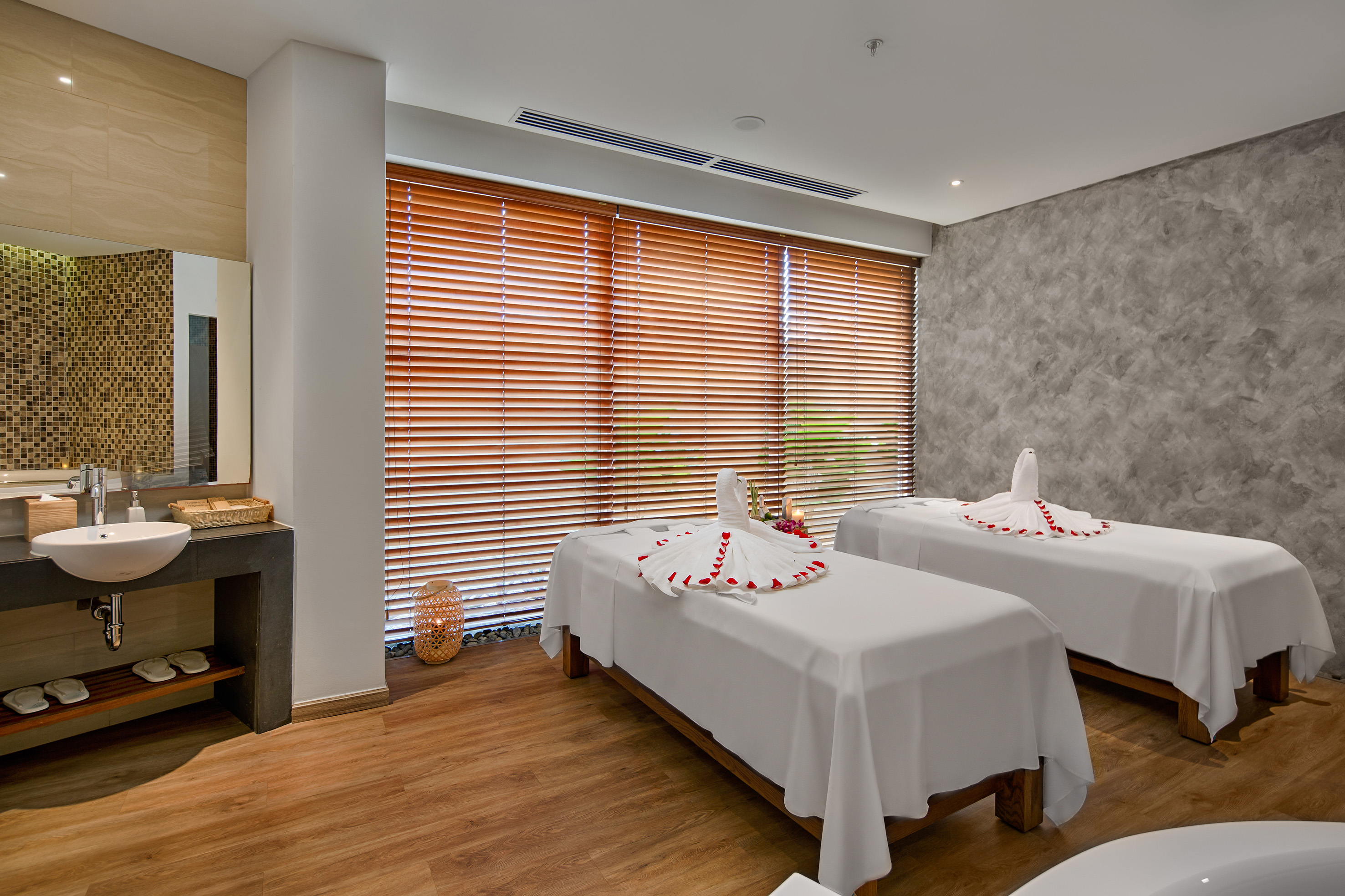 Serene spa room with two massage beds, swan towels, and wooden blinds.