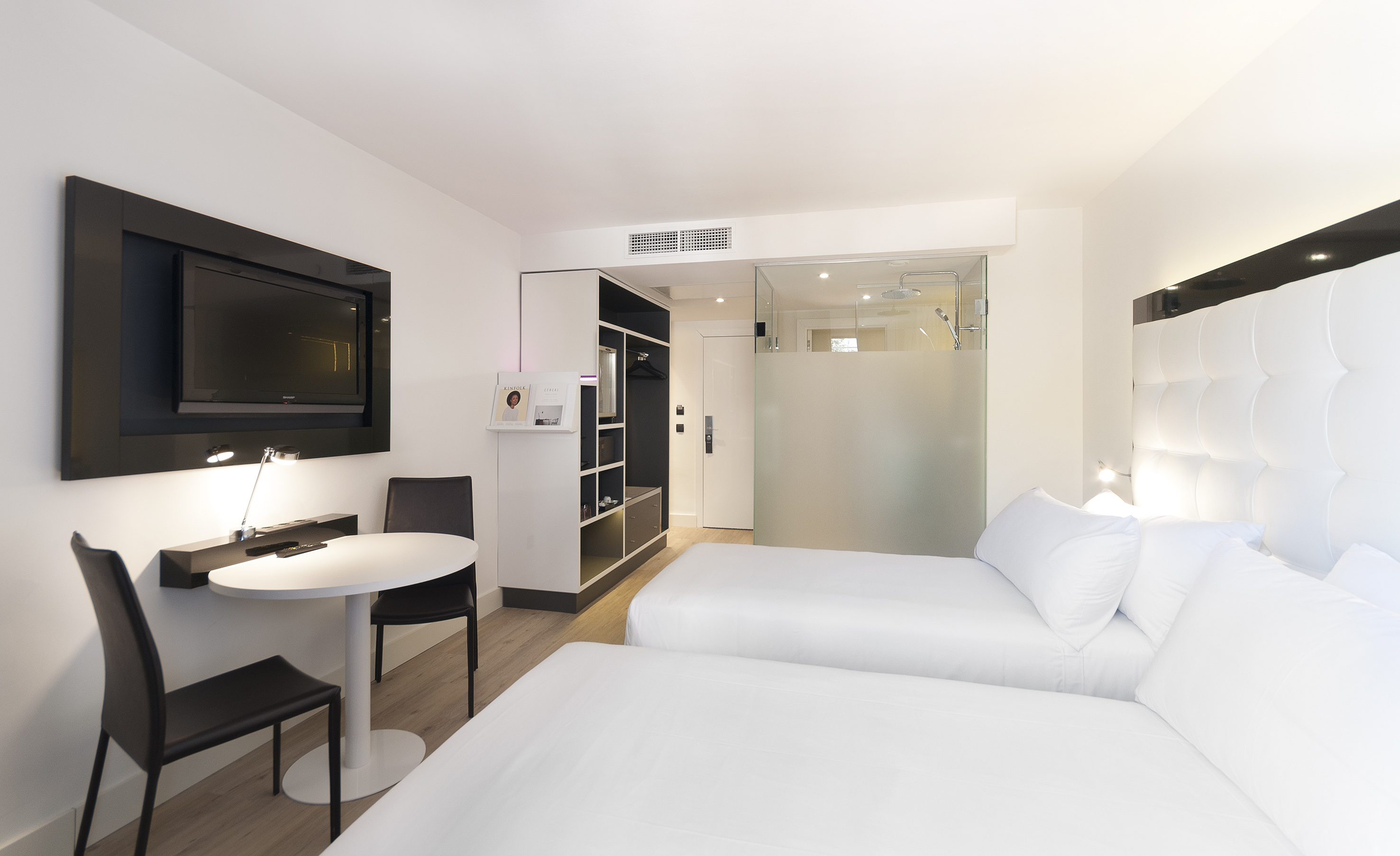 Modern hotel twin room with white beds, wall TV, and glass shower.