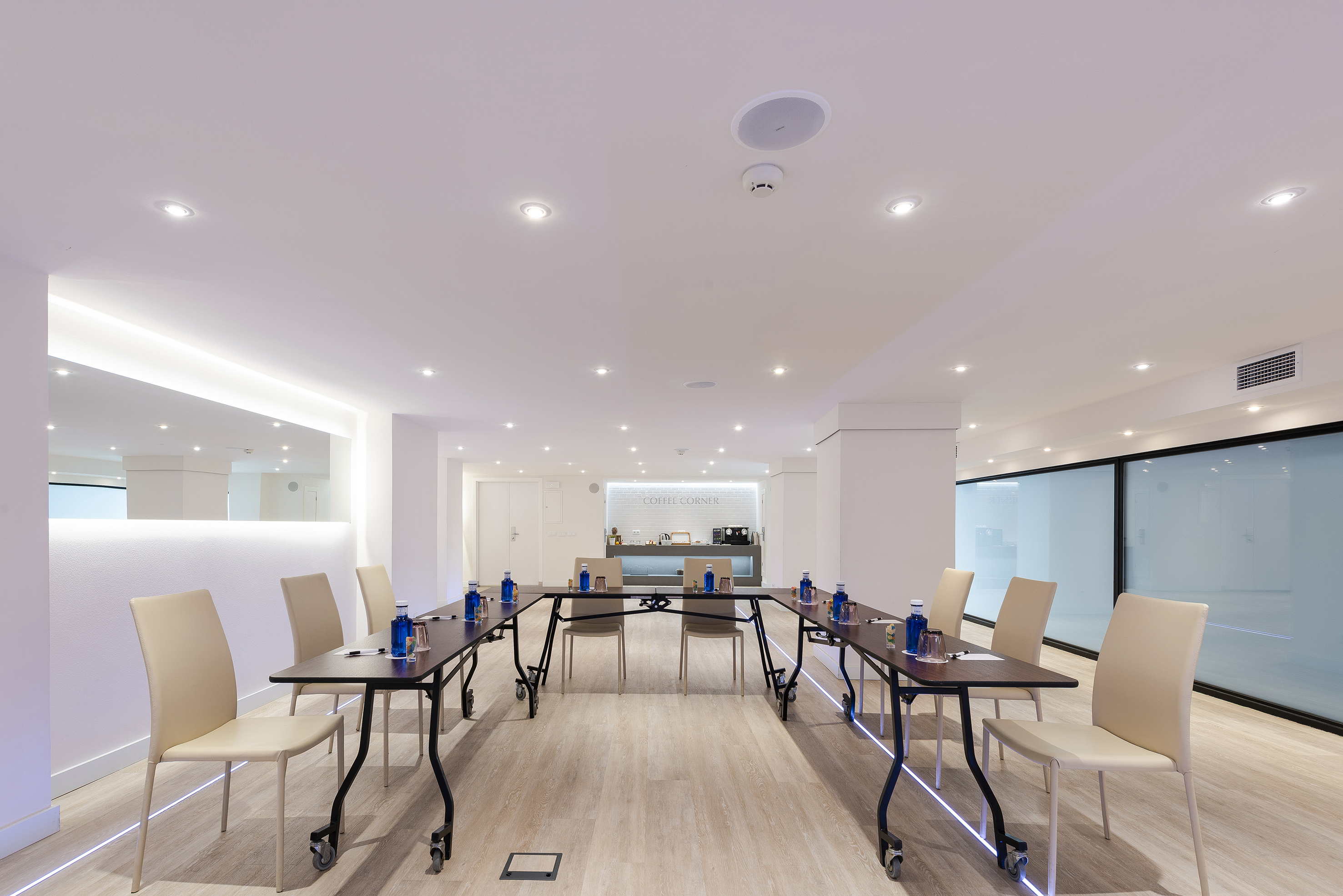 Modern hotel meeting room with U-shaped tables and a coffee corner.