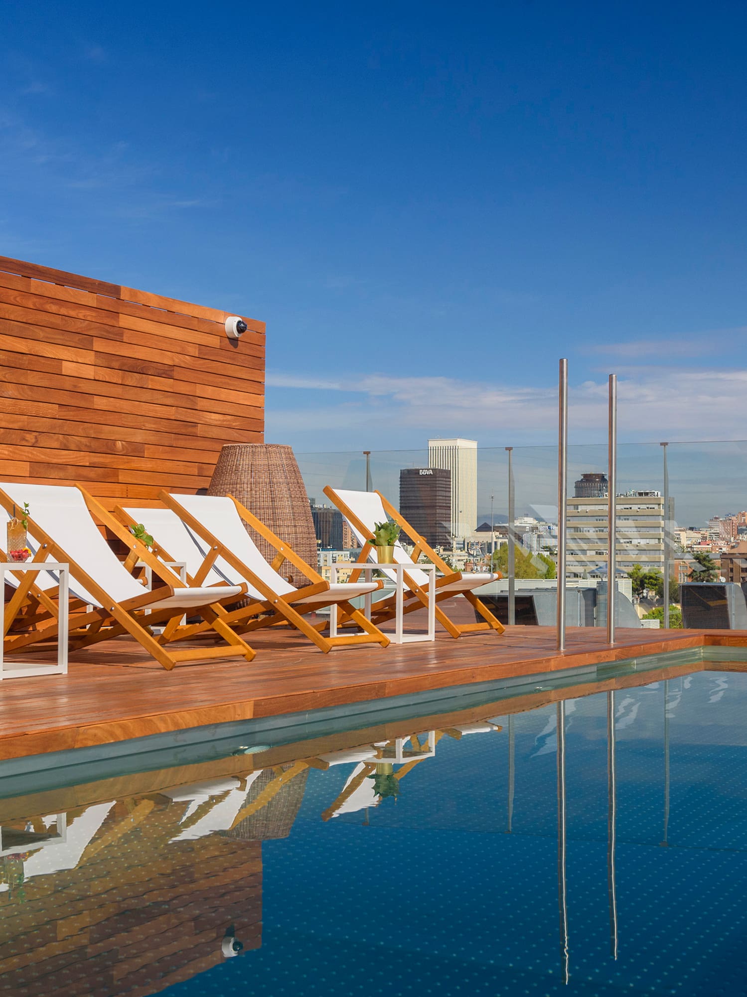 Rooftop pool deck with lounge chairs and city skyline view.