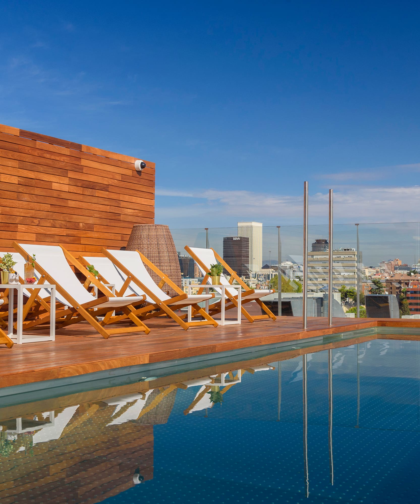 Rooftop pool deck with lounge chairs and city skyline view.