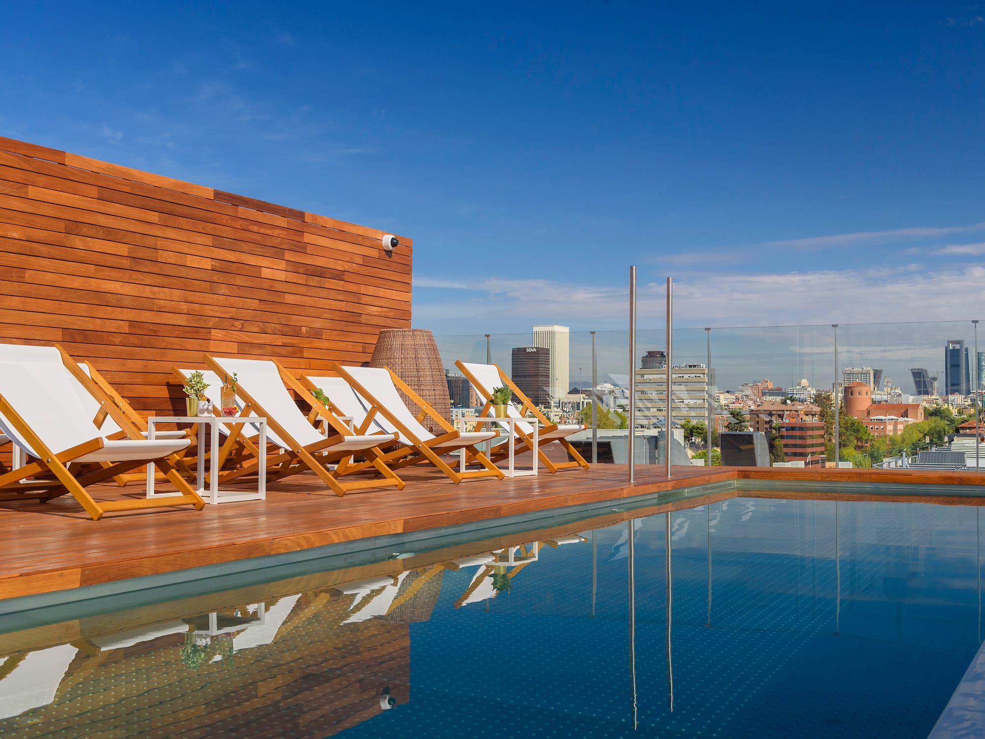 Rooftop pool deck with lounge chairs and city skyline view.