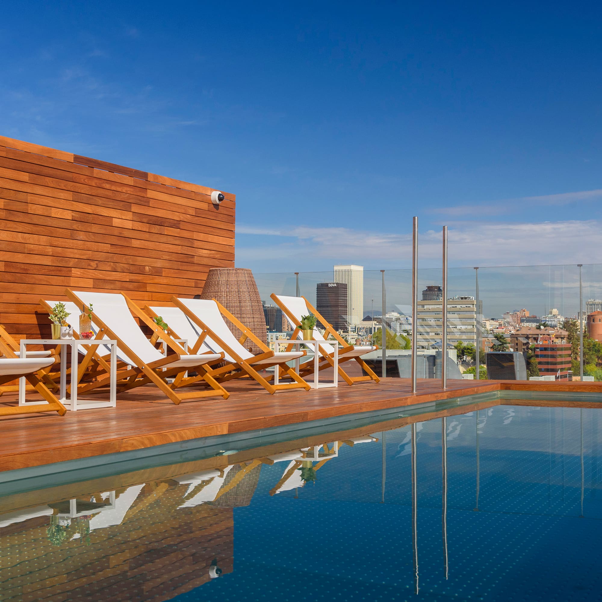 Rooftop pool deck with lounge chairs and city skyline view.
