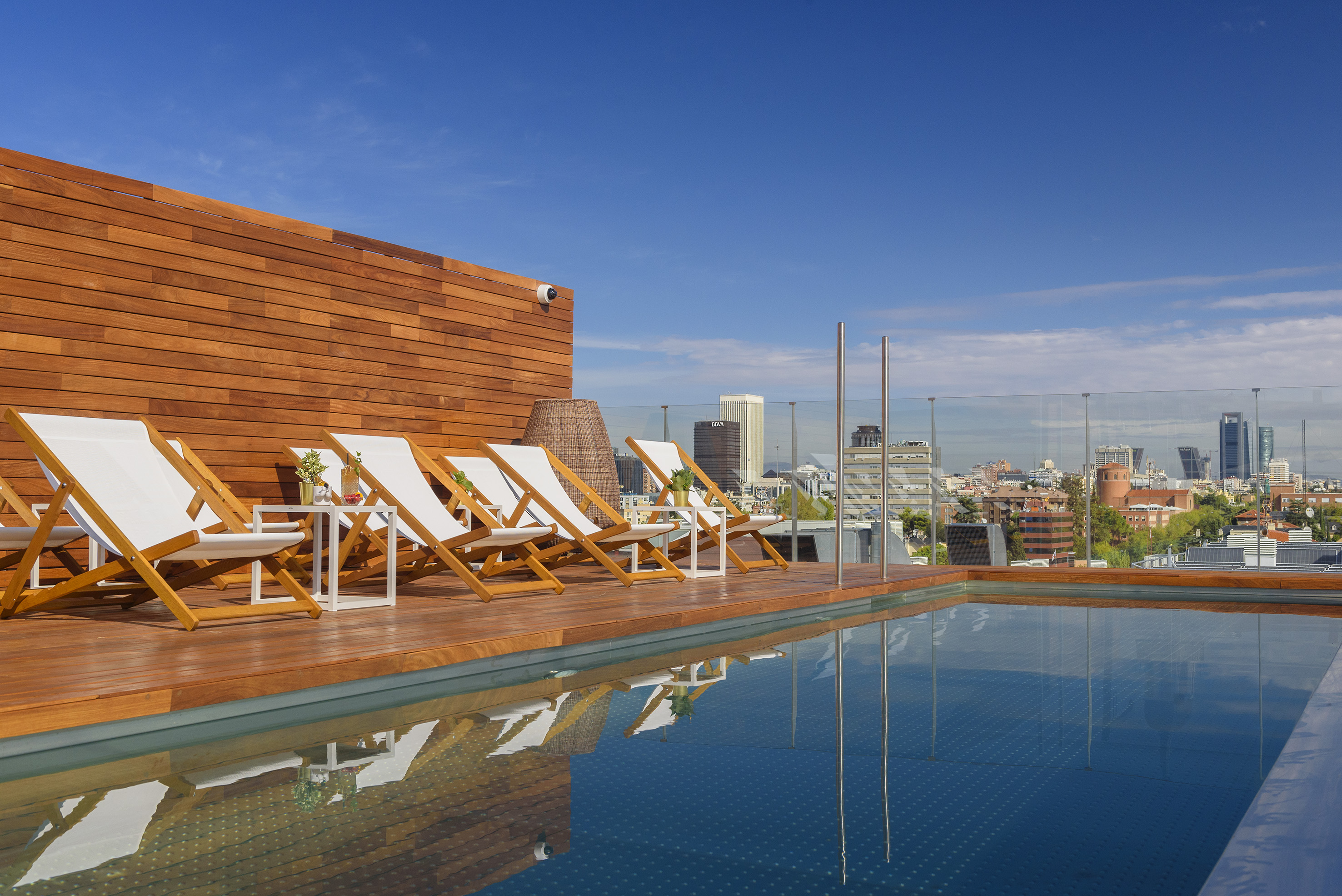 Rooftop pool deck with lounge chairs and city skyline view.