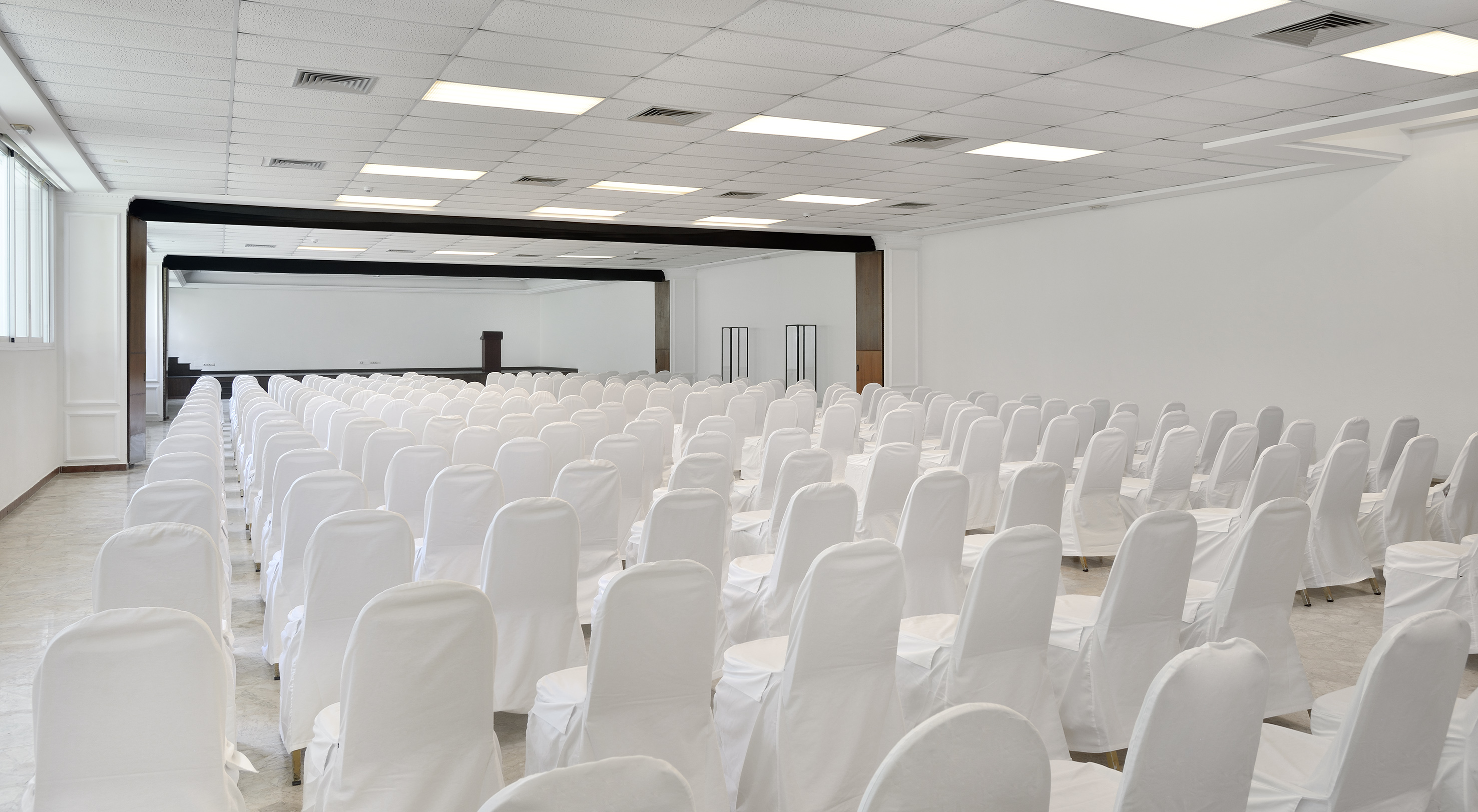 Empty conference hall with rows of white covered chairs and stage.