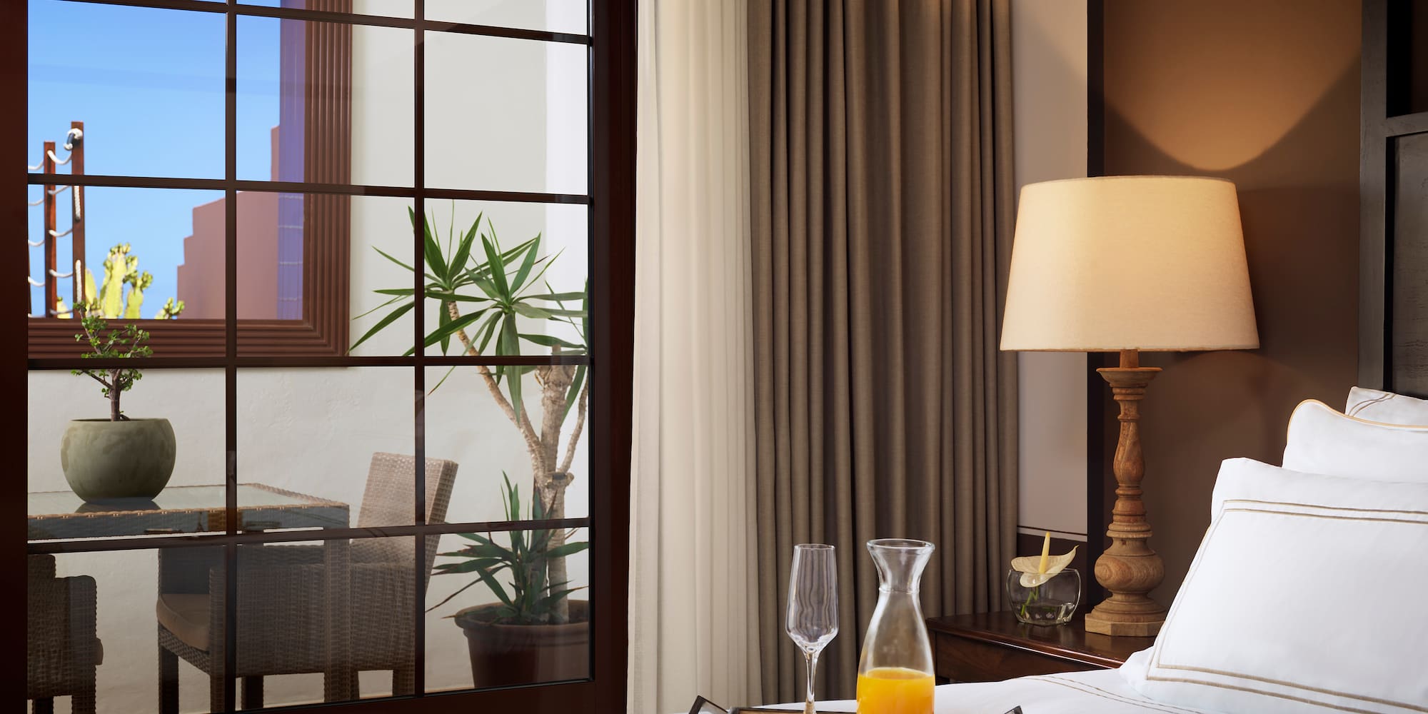 a bed with a tray of juice and a lamp in front of a window