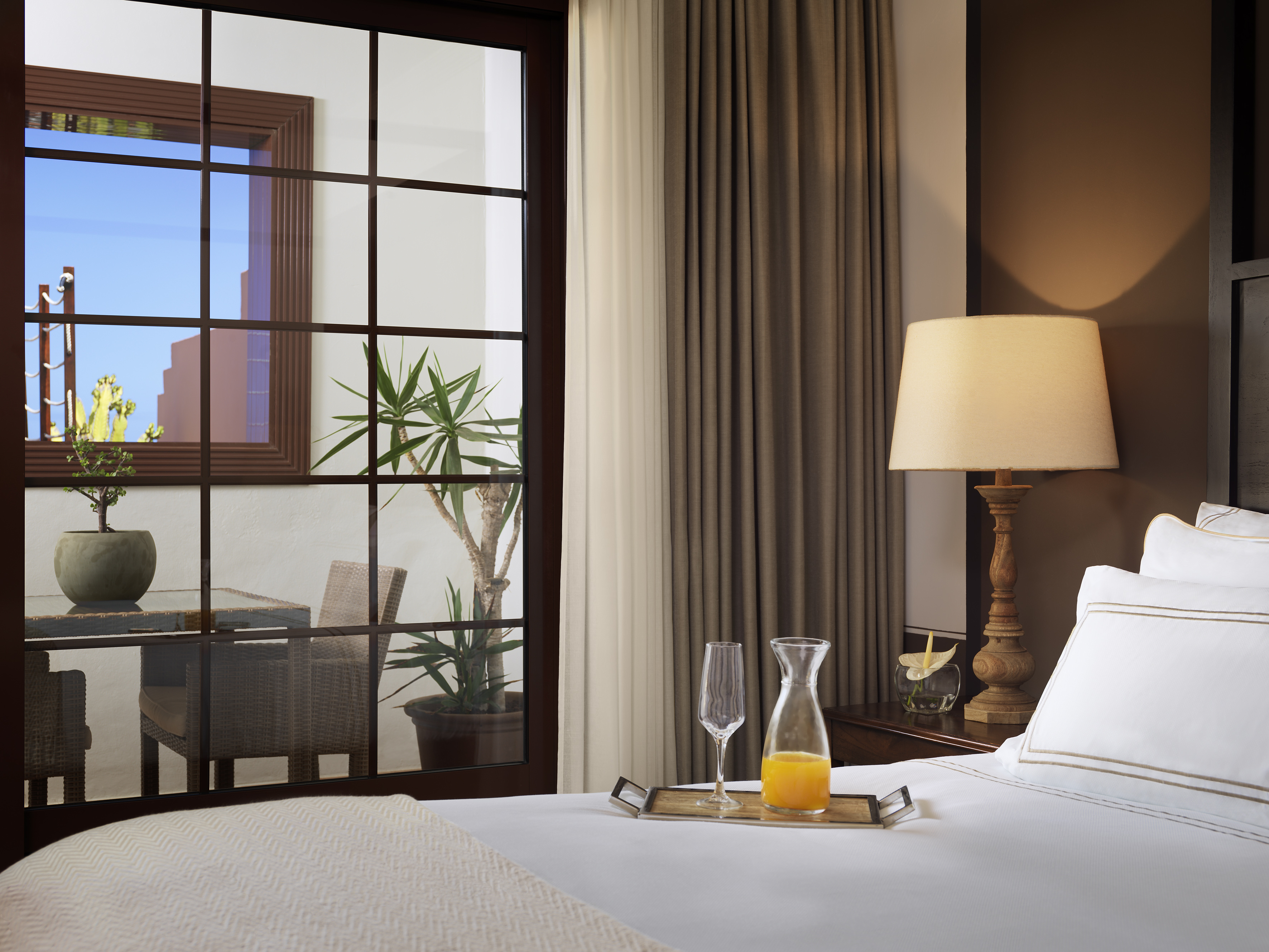 a bed with a tray of juice and a lamp in front of a window