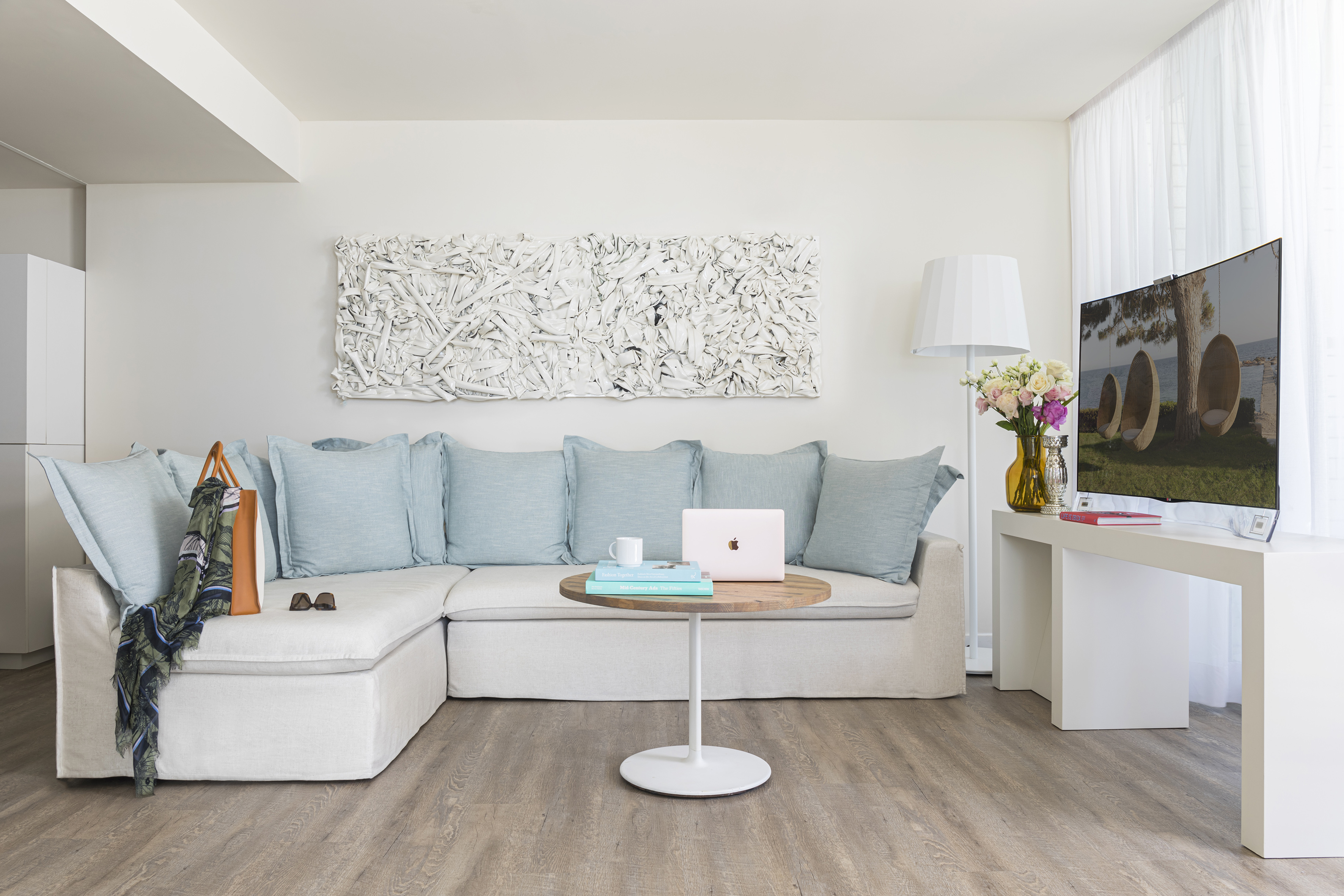 Modern living room, L-shaped sofa, blue cushions, textured wall art, and laptop.