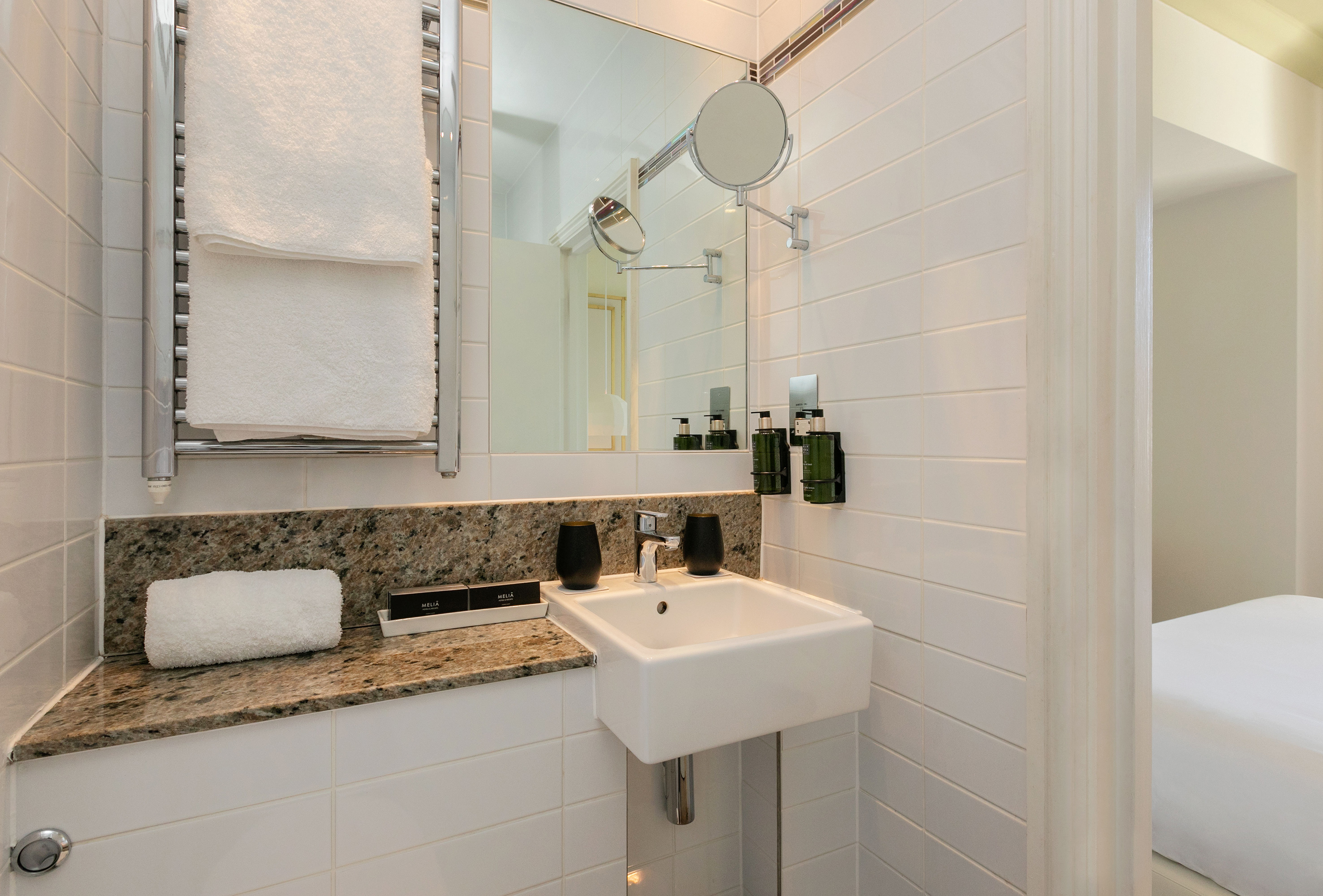 Hotel bathroom with white sink, granite counter, mirror, and fresh towels.