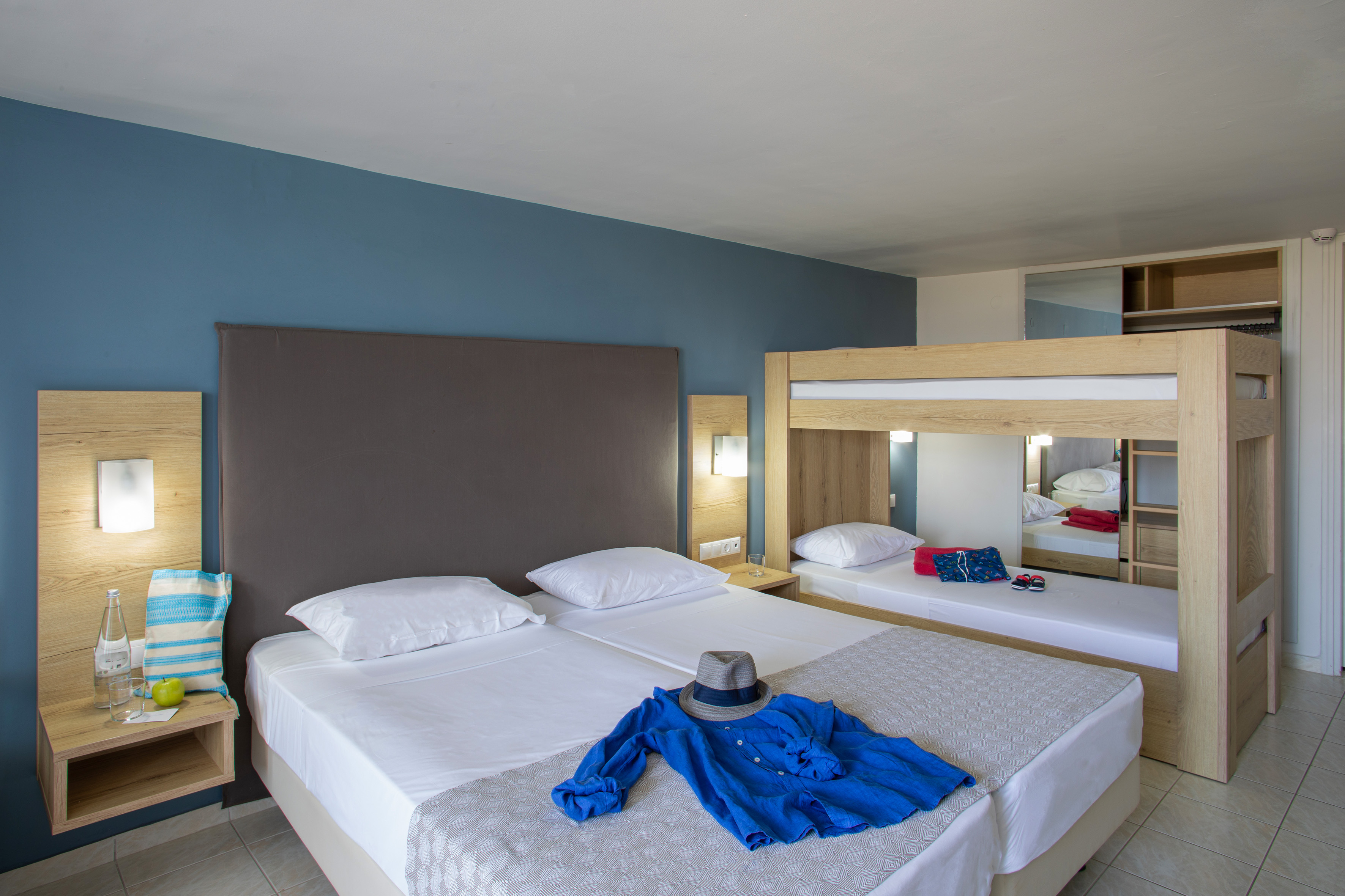Hotel family room with twin beds and bunk beds, blue wall, wooden decor.