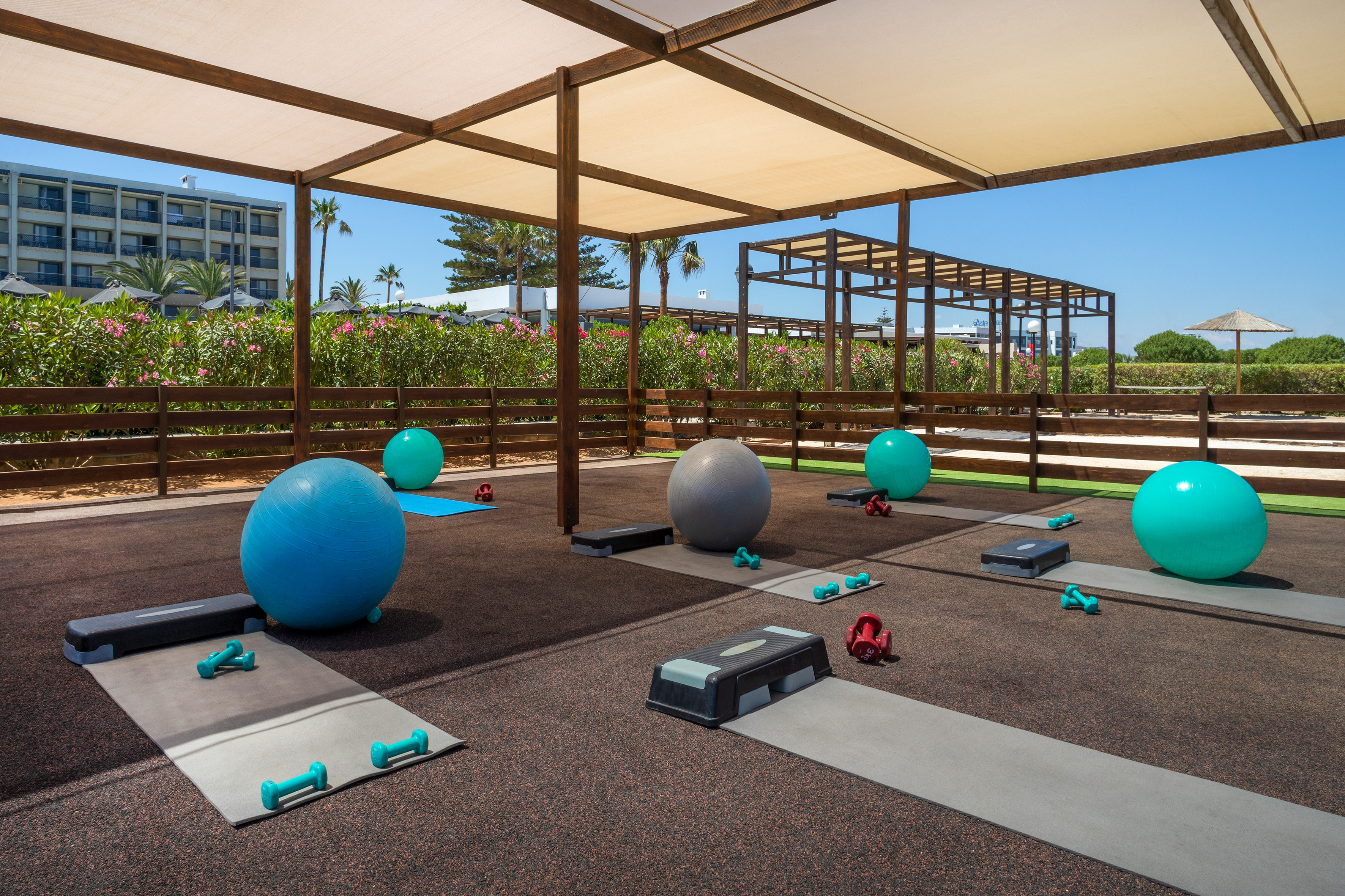 Outdoor resort gym with fitness balls, mats, and dumbbells under shade.